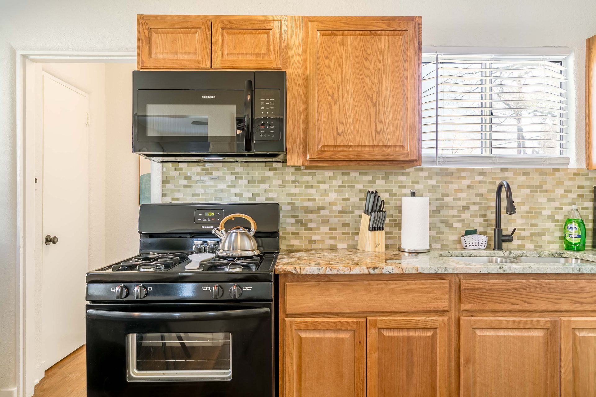 A kitchen with a stove , microwave , sink and wooden cabinets.