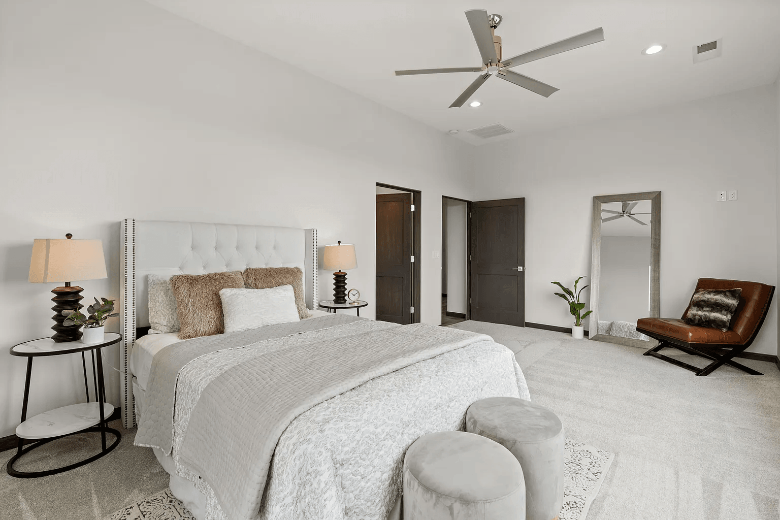 A bedroom with a bed , chair , lamps and a ceiling fan.