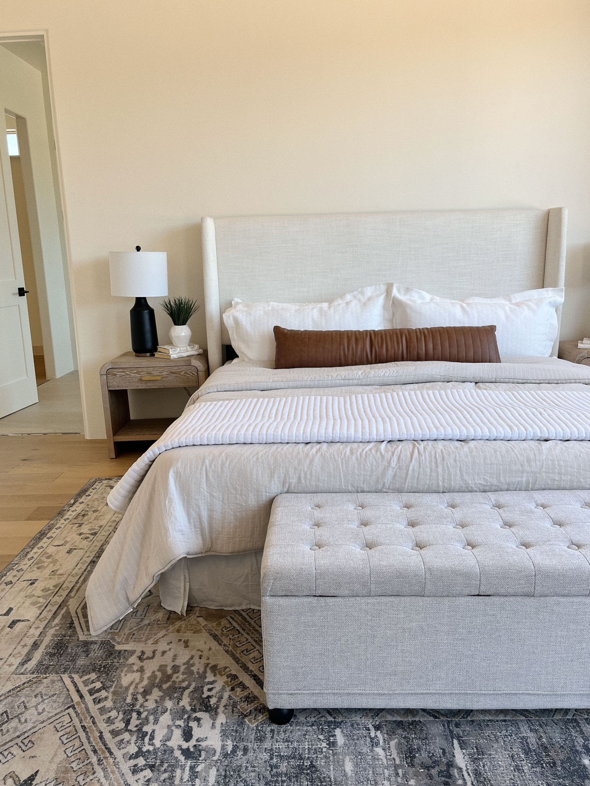 A bedroom with a bed , ottoman , nightstand and rug.