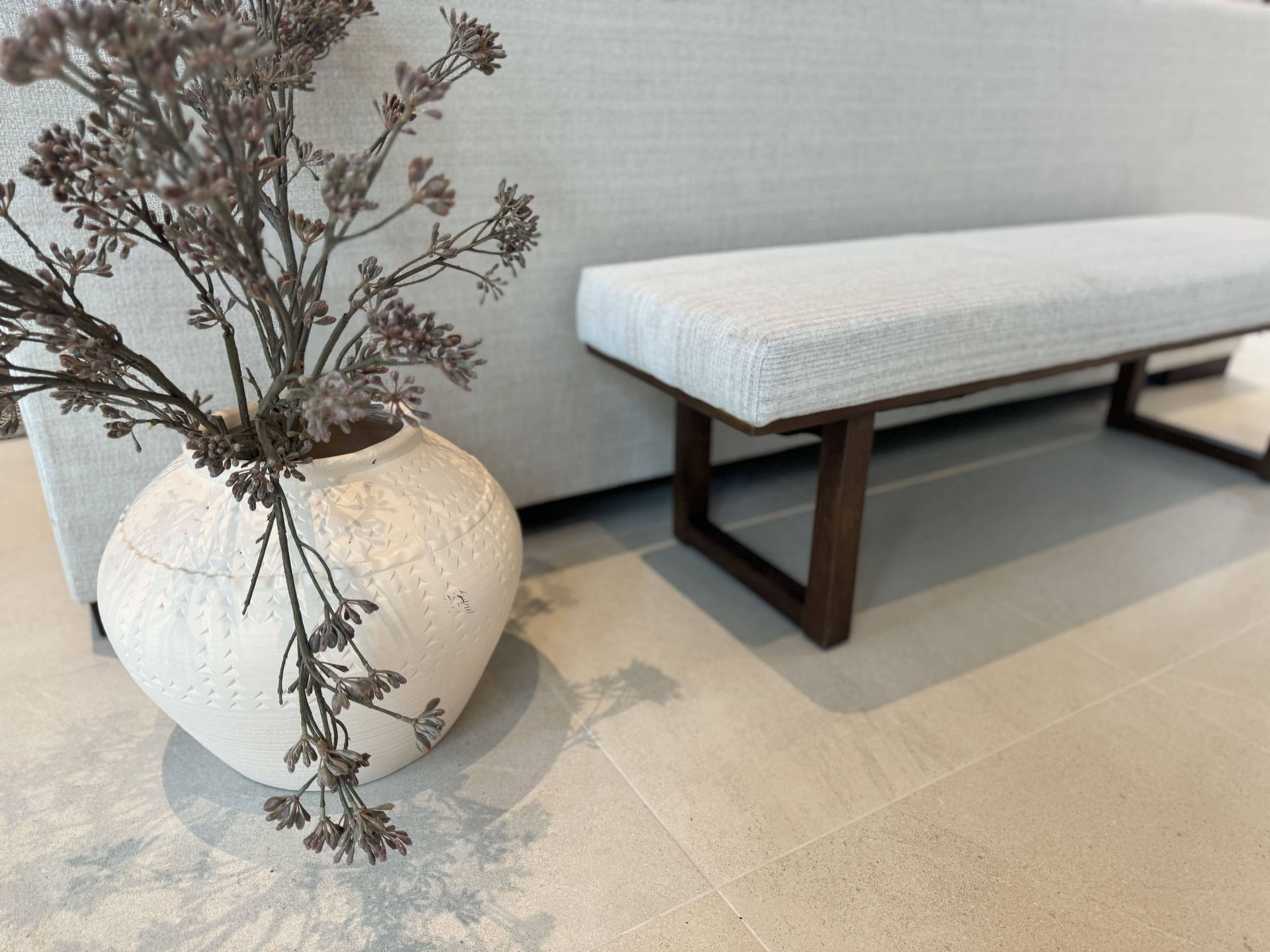 A vase of flowers sits next to a bench in a living room.