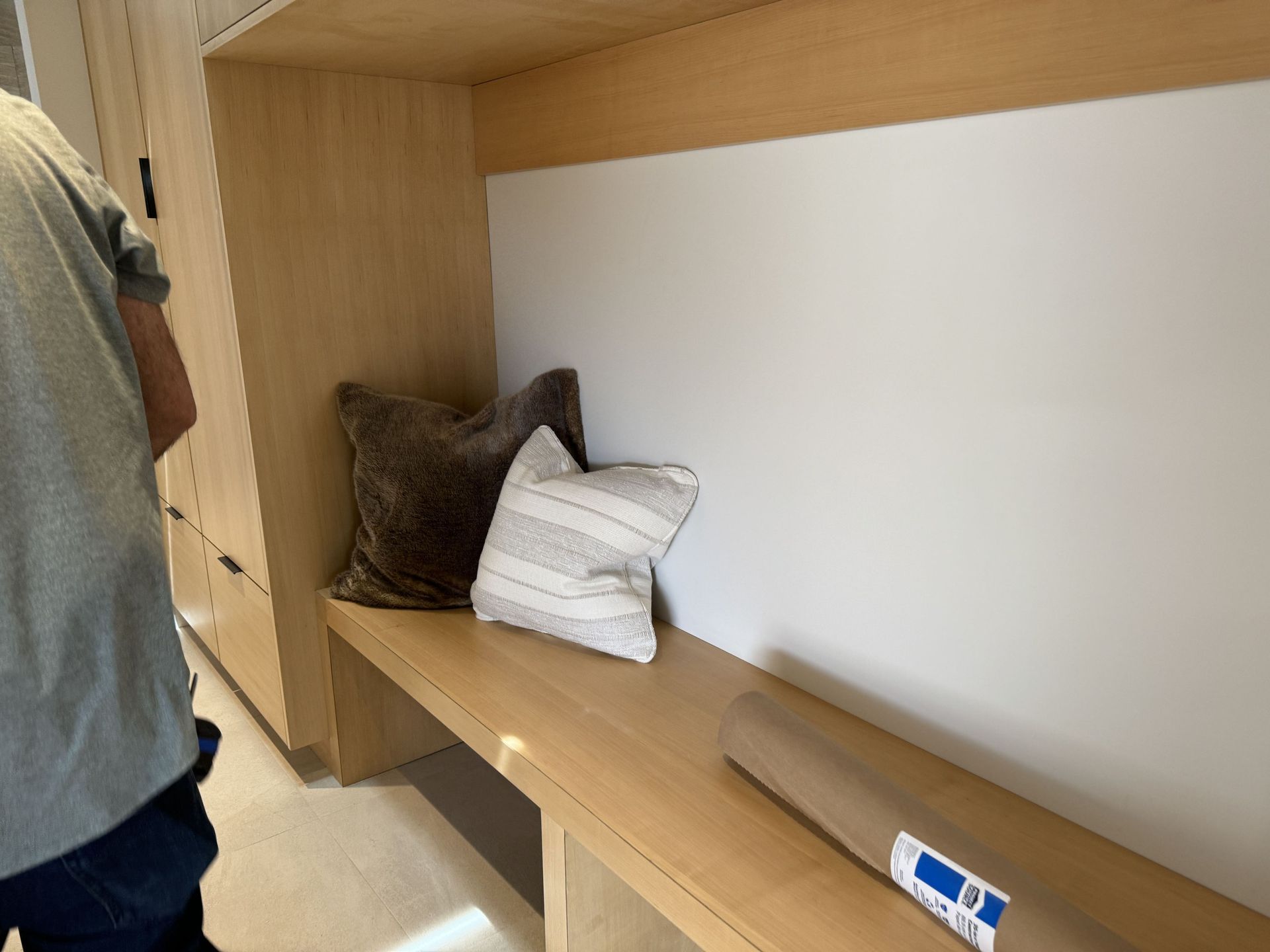A person is standing next to a wooden bench with a pillow on it.