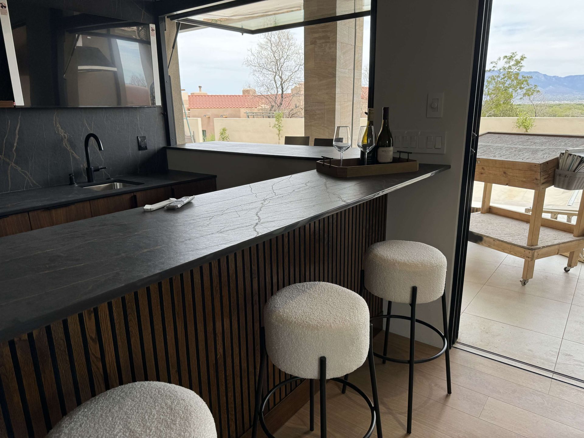 A kitchen with a bar and stools and a bottle of wine on the counter.