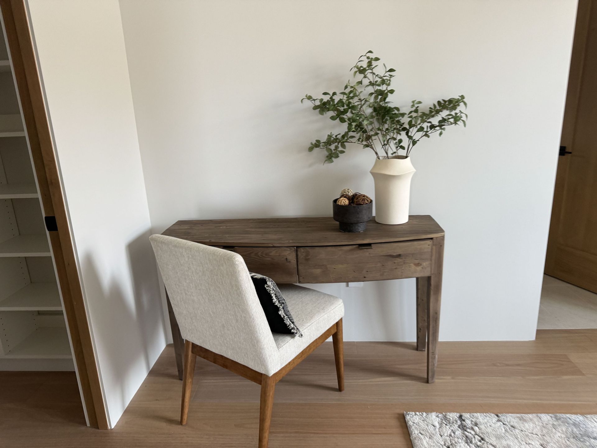 A desk with a chair and a vase on it in a room.