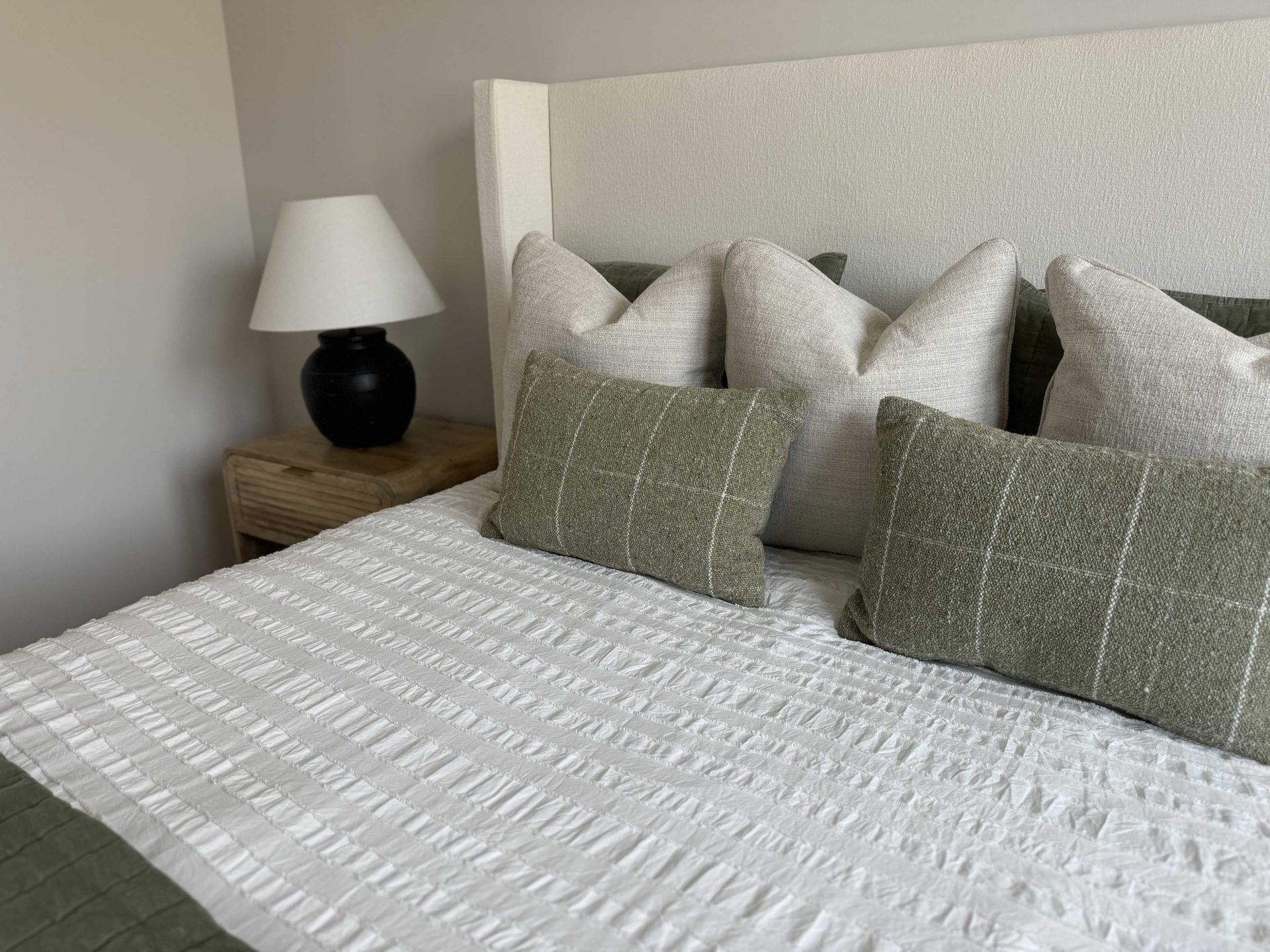 A bedroom with a bed , nightstand , lamp and pillows.