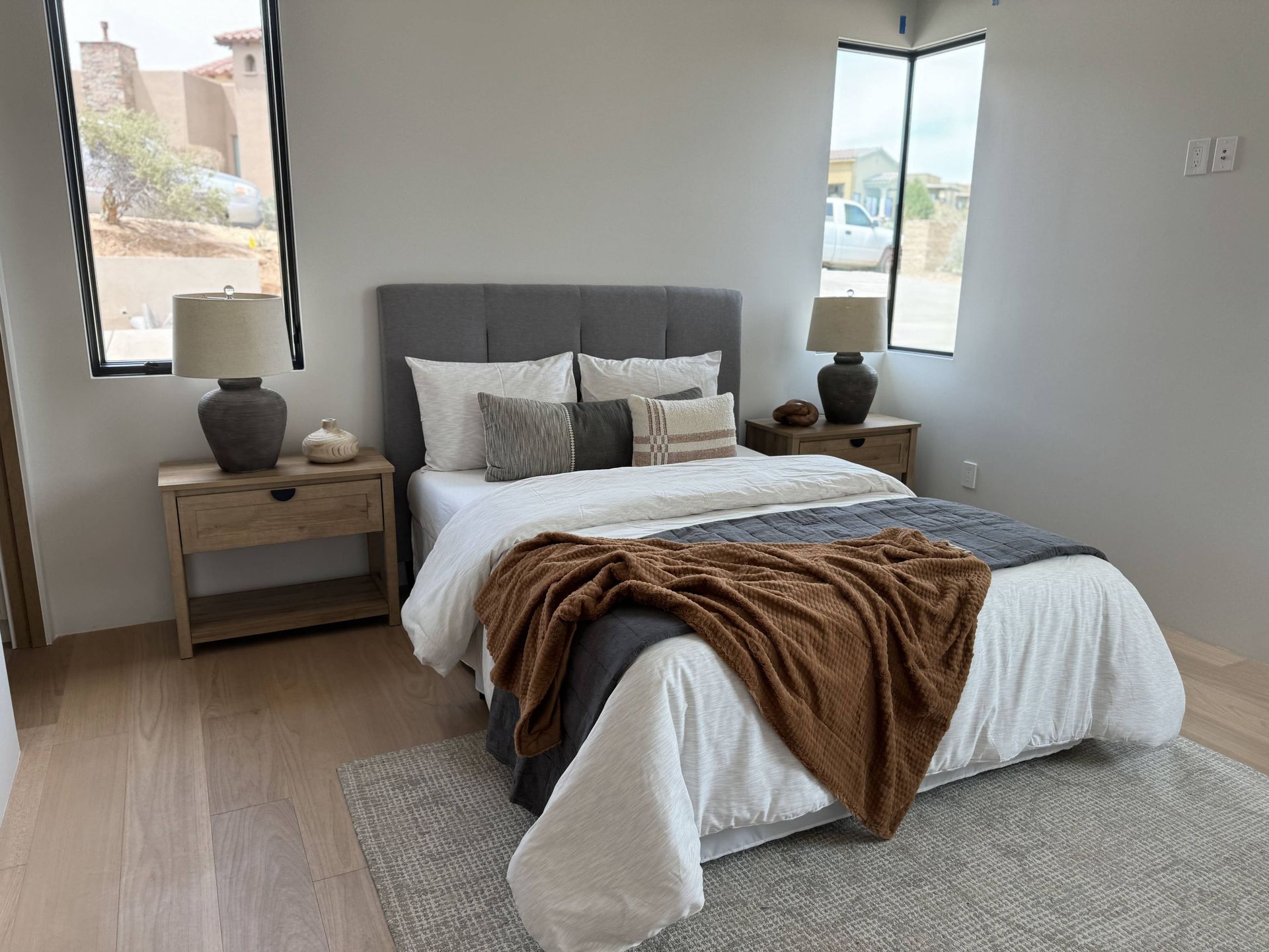A bedroom with a bed , nightstands , lamps and two windows.