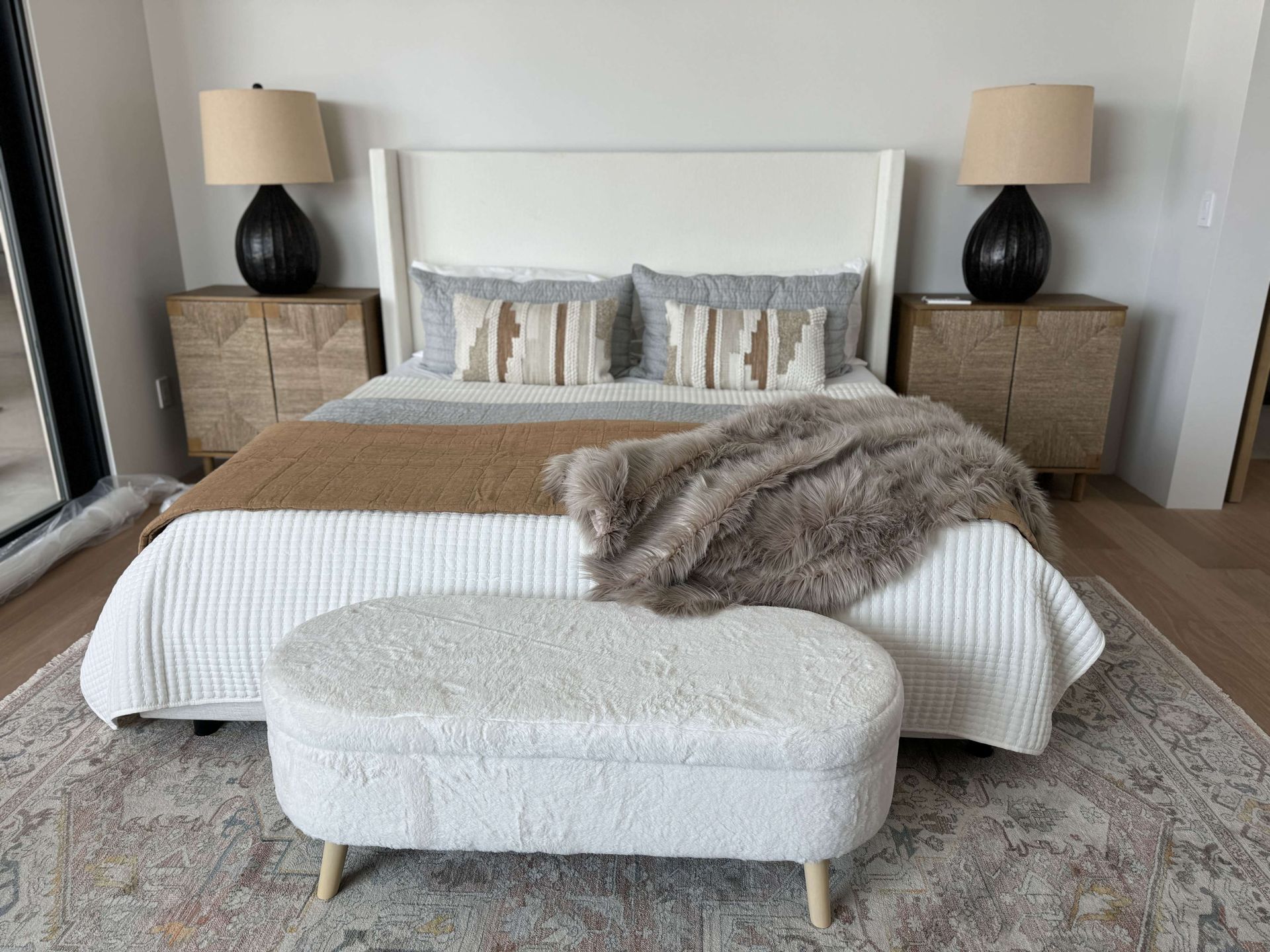 A bedroom with a bed , nightstands , lamps and a bench.