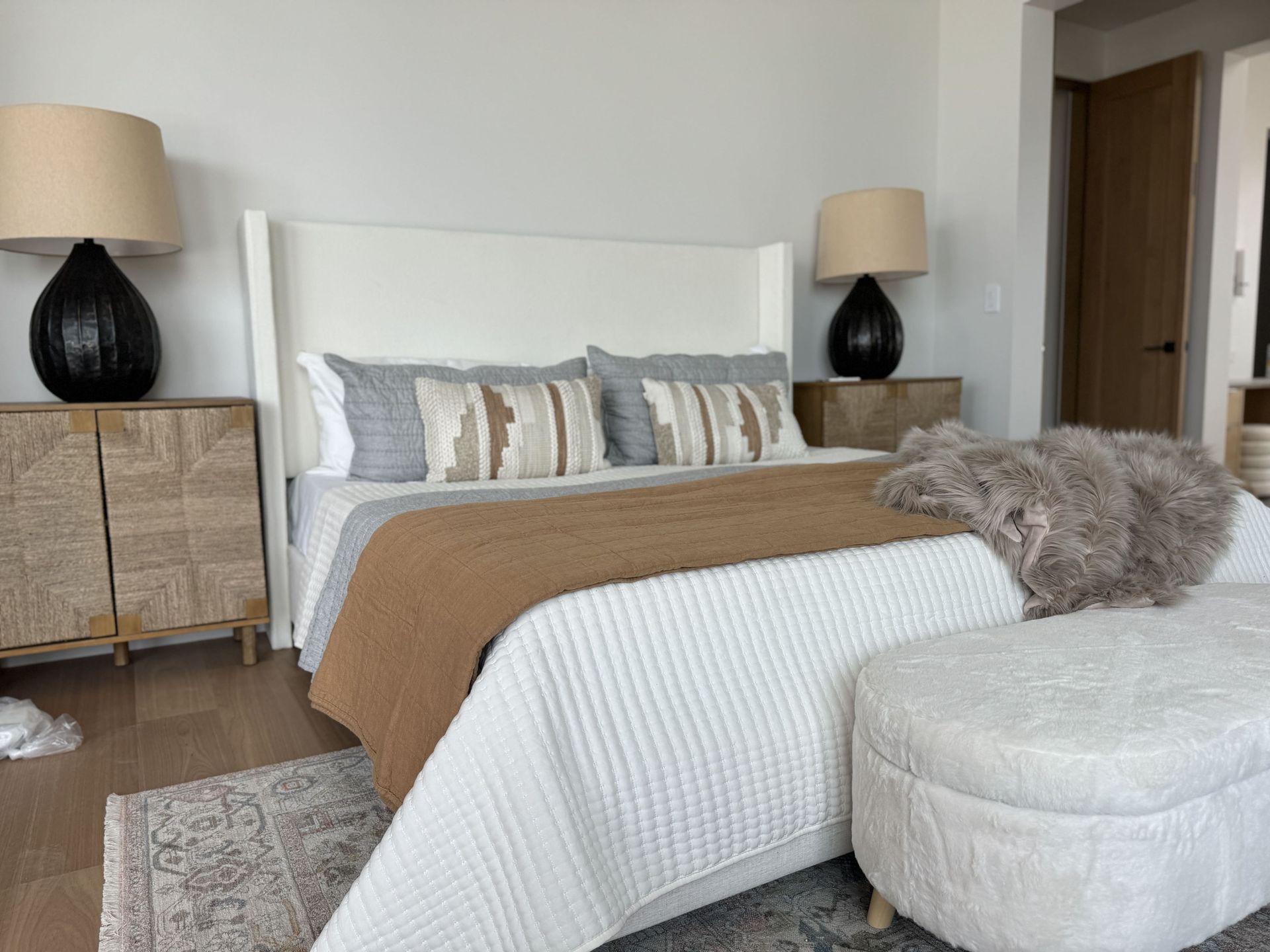 A bedroom with a bed , lamps , nightstands and an ottoman.