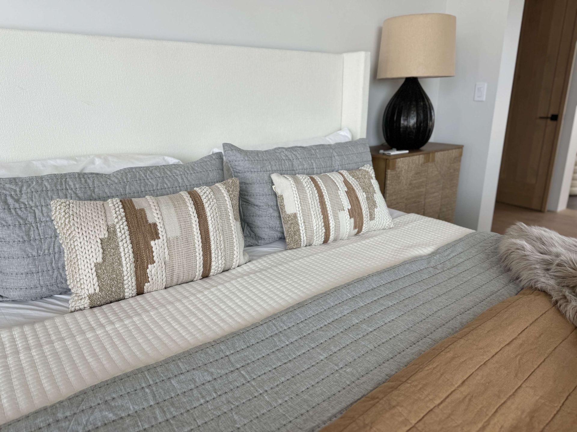 A bedroom with a bed , nightstand , lamp and pillows.