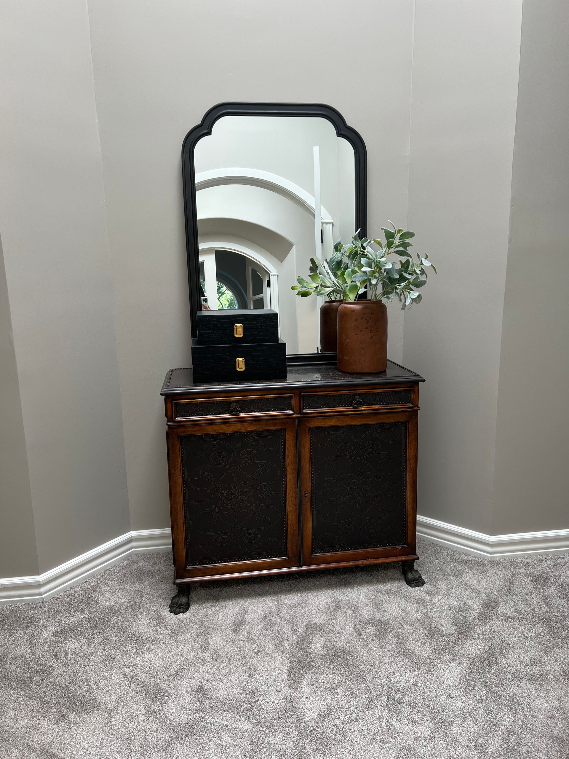 A mirror is sitting on top of a wooden dresser in a corner of a room.
