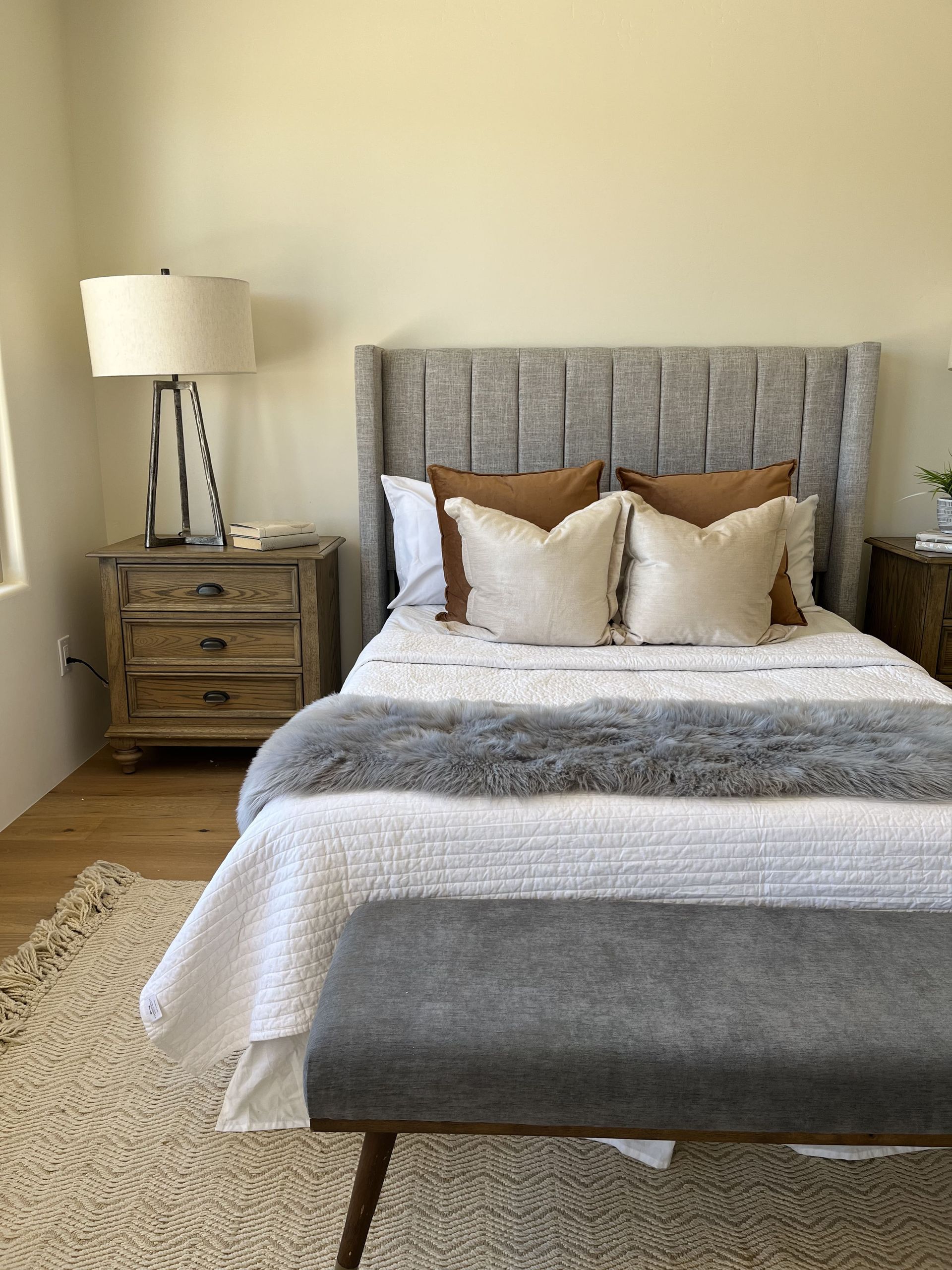A bedroom with a bed , nightstand , lamp and bench.