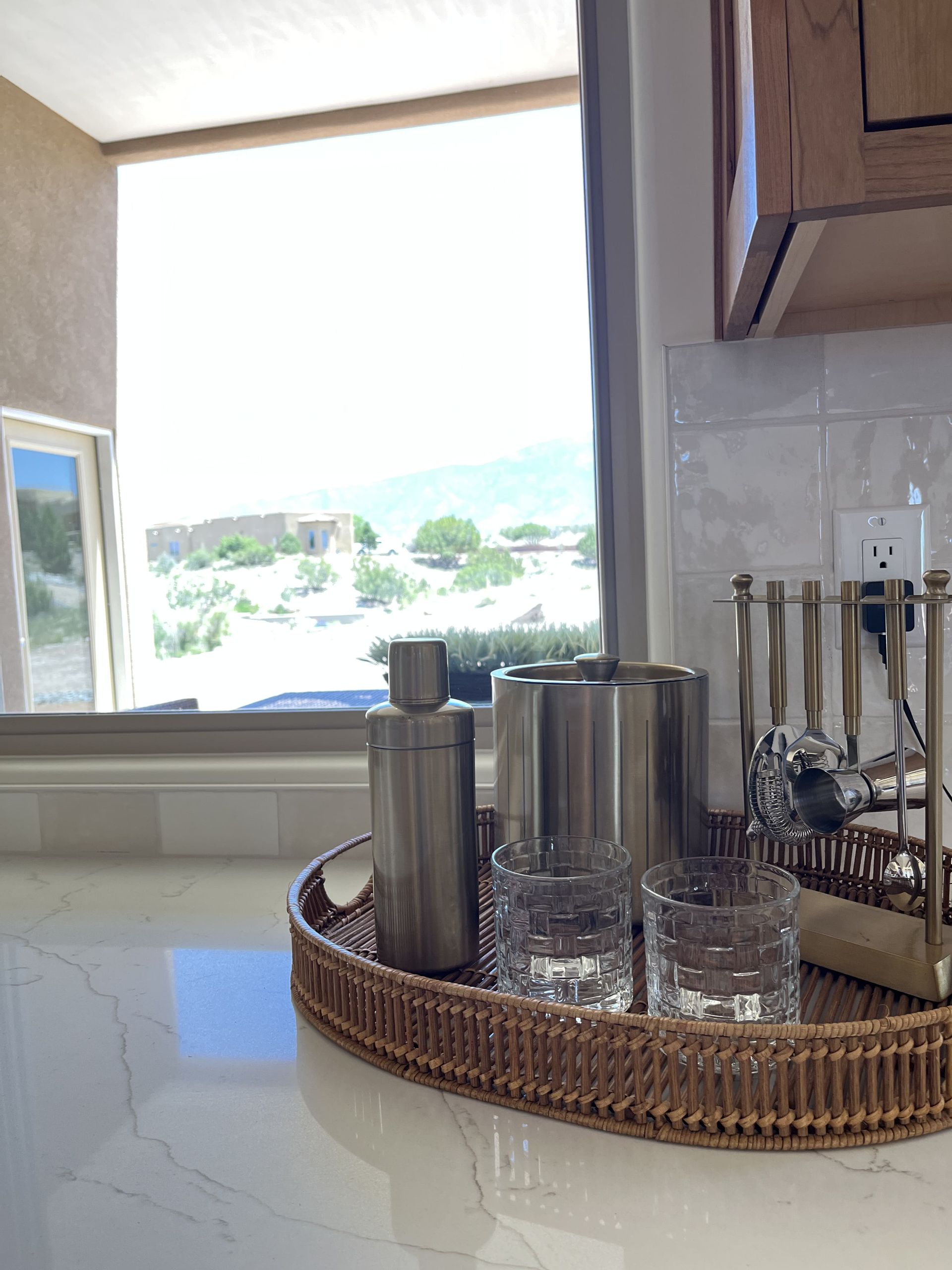 A kitchen counter with a wicker tray filled with glasses and utensils.