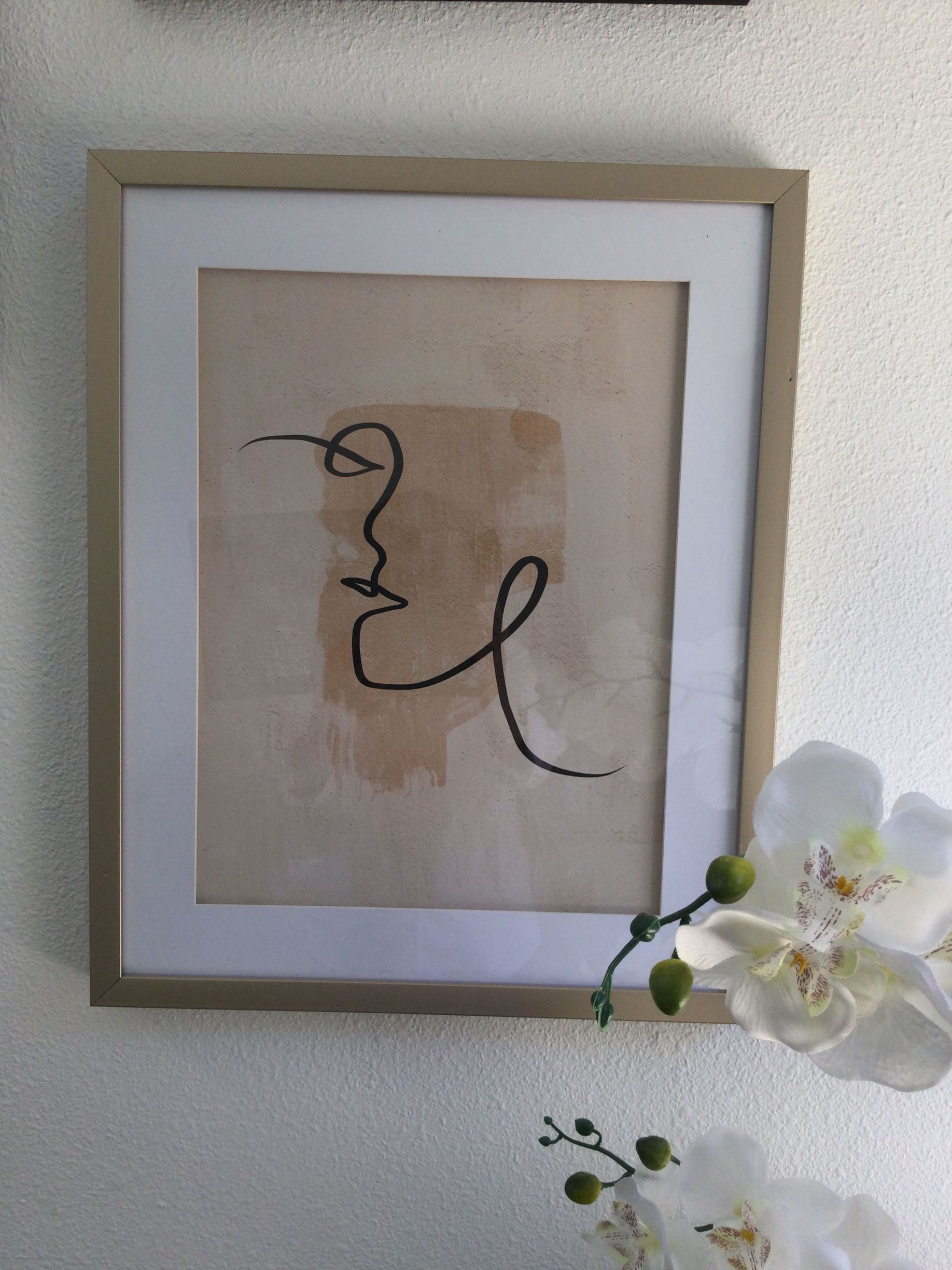 A framed drawing of a woman 's face is hanging on a wall
