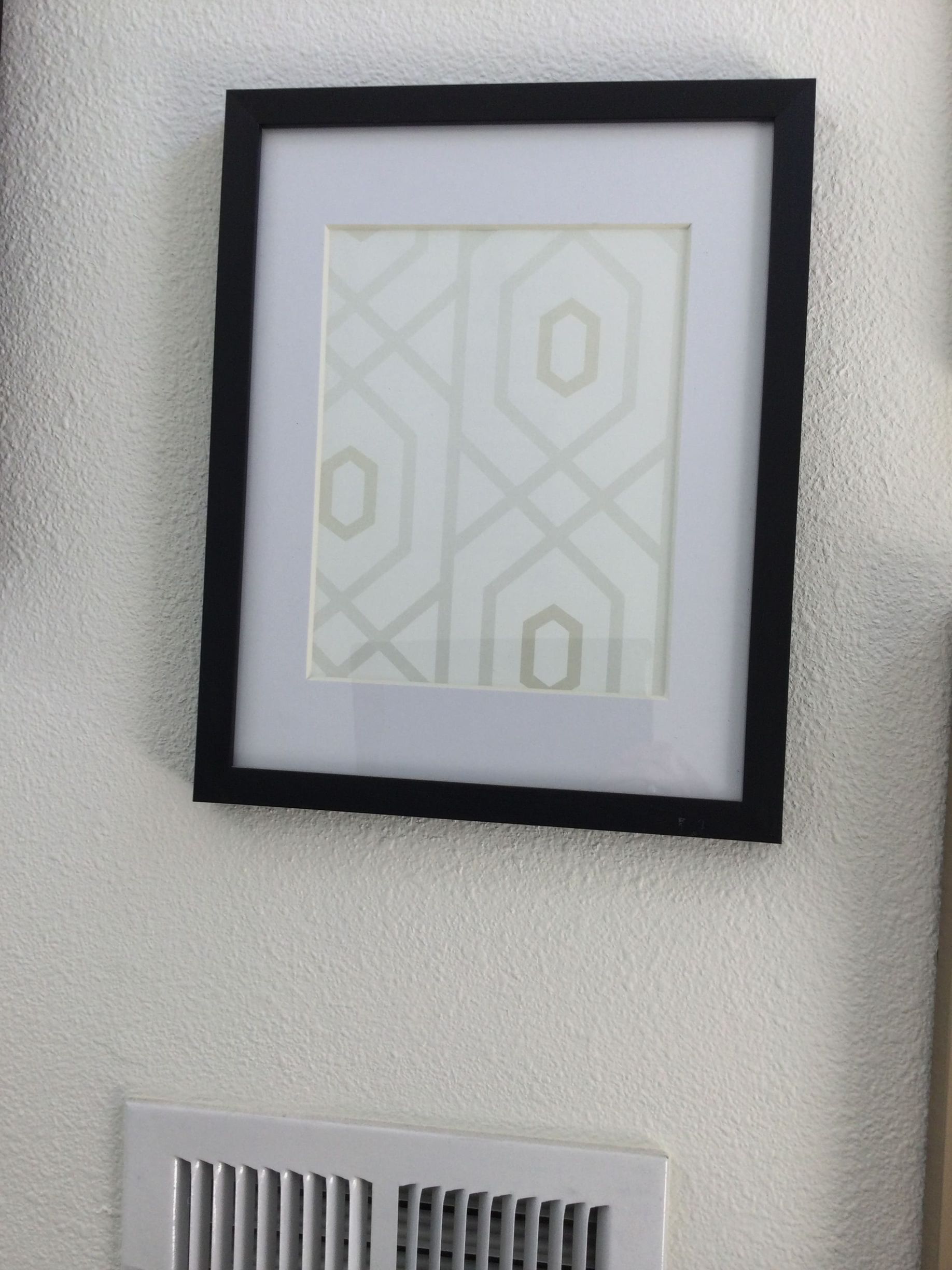 A picture in a black frame hangs on a white wall