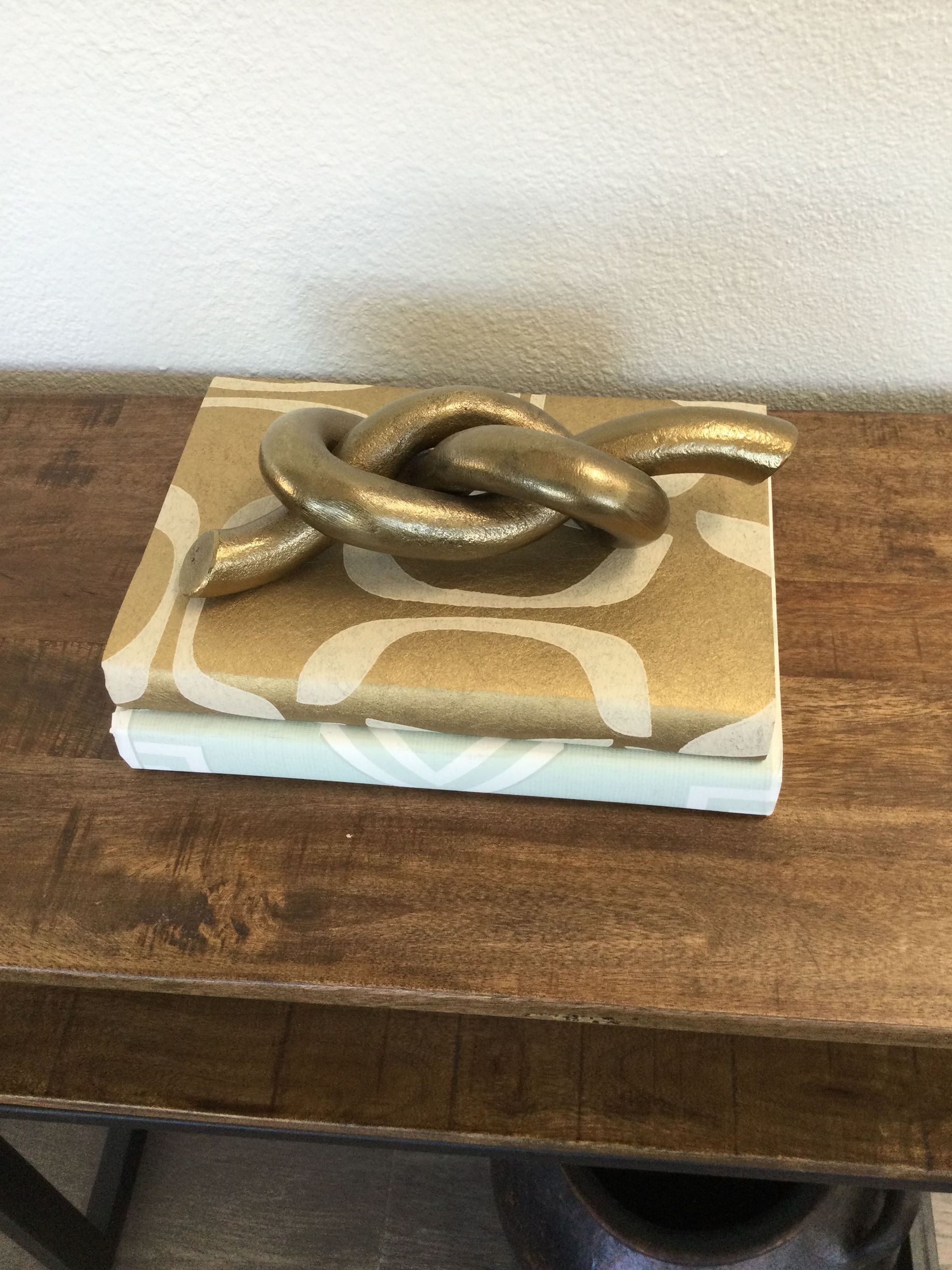 A sculpture of a knot is sitting on top of a stack of books on a wooden table.