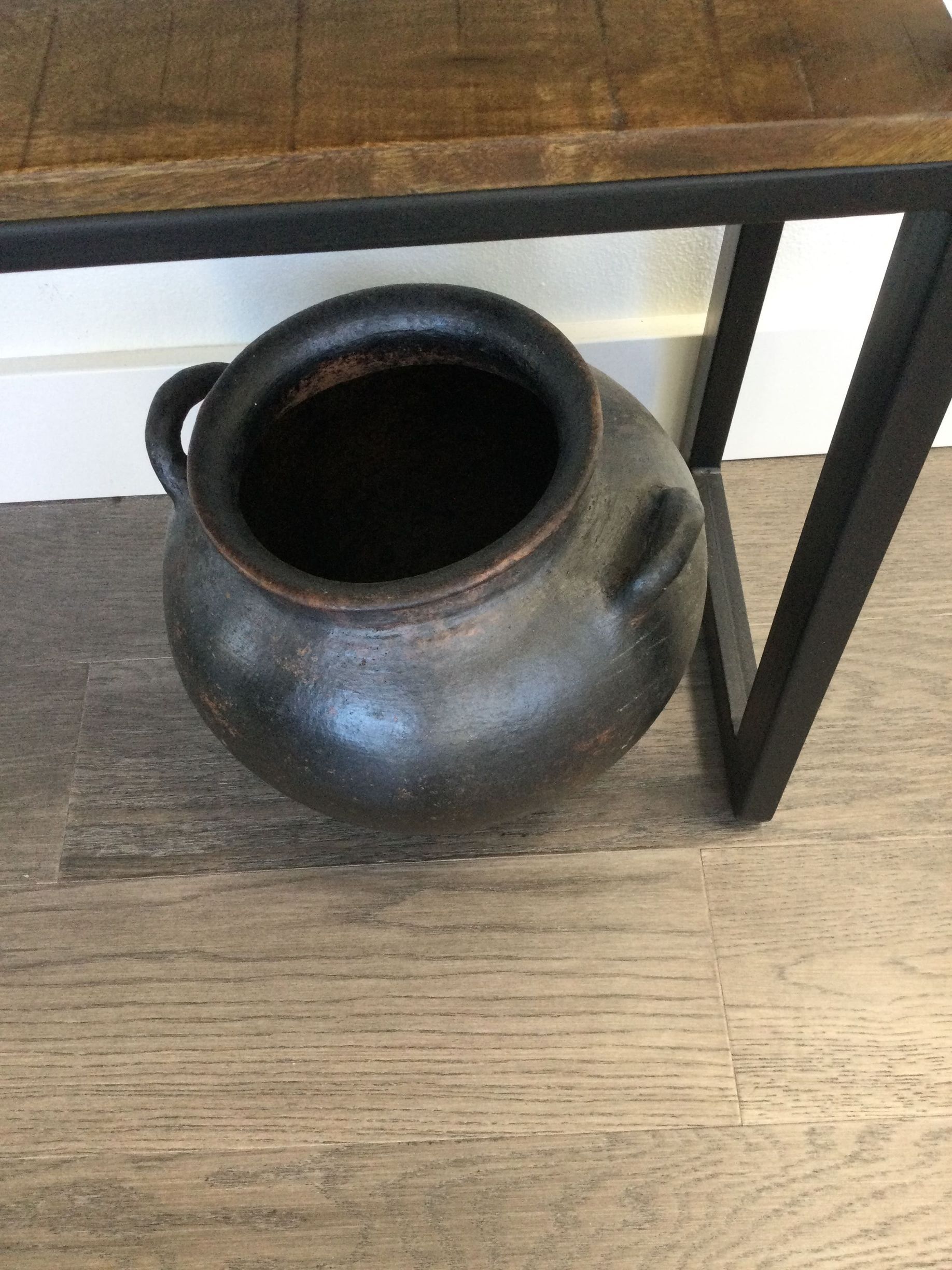 A black pot is sitting on a wooden table.