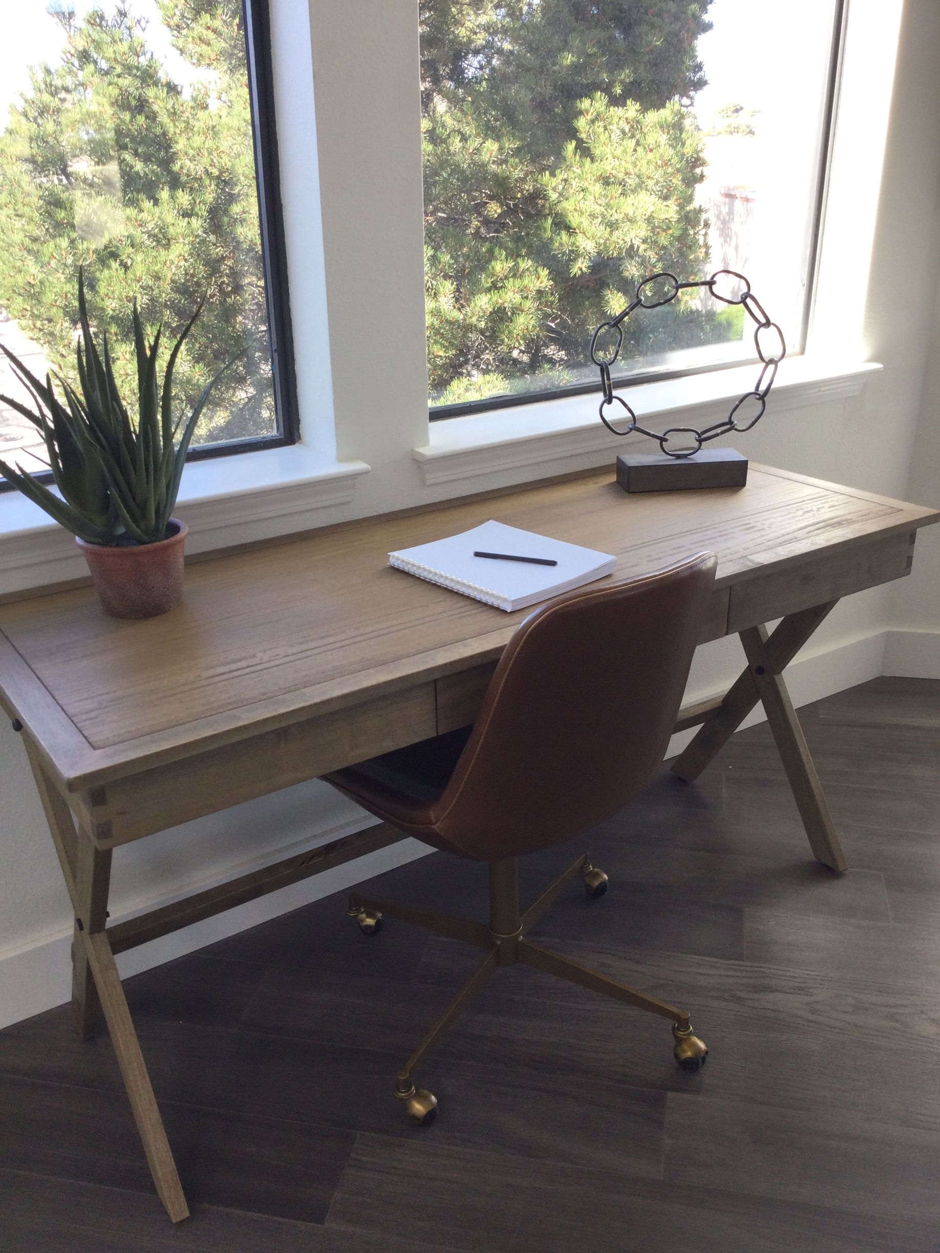 A desk with a chair and a plant on it in front of a window.