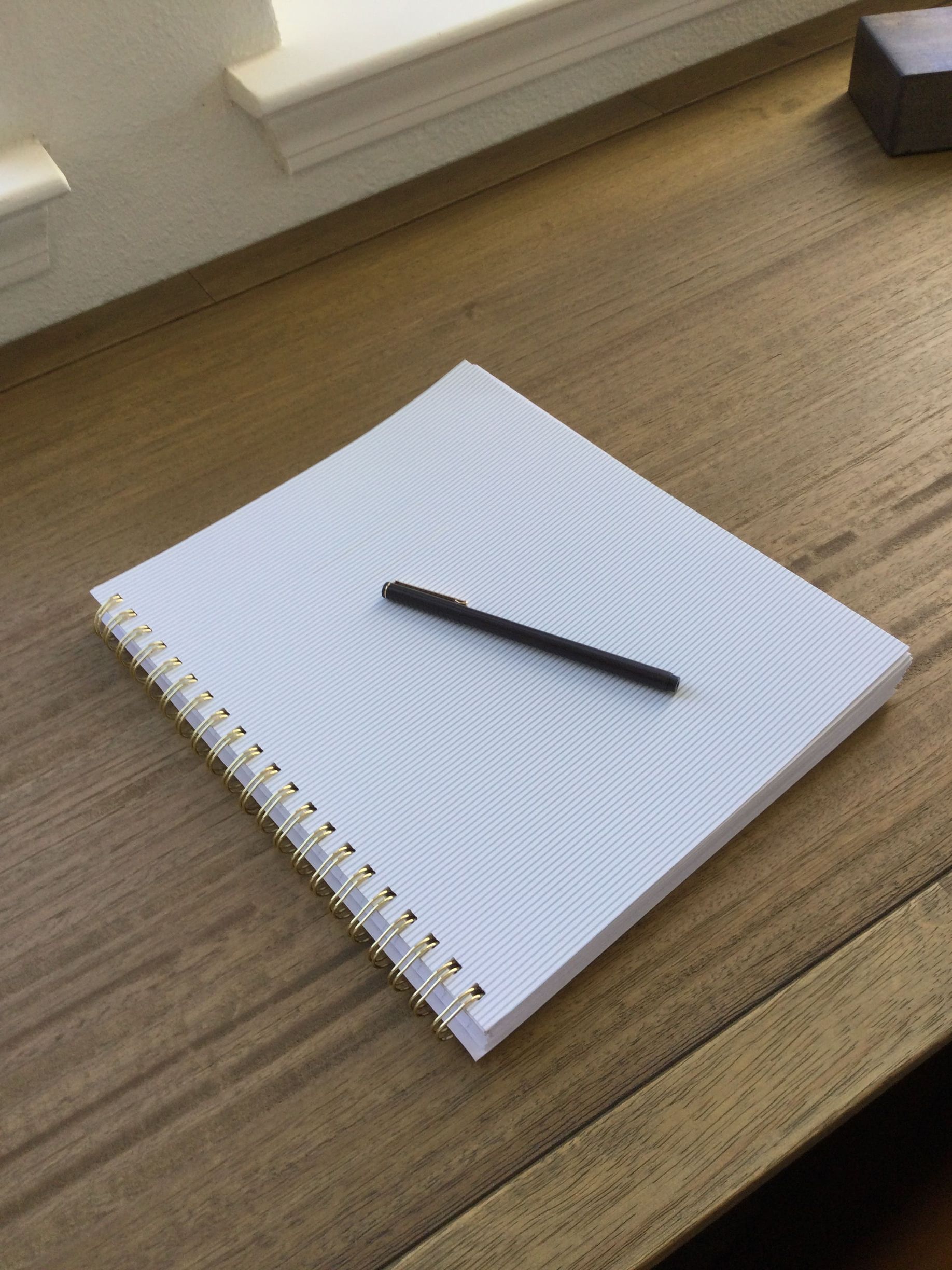 A notebook and pen are on a wooden table.
