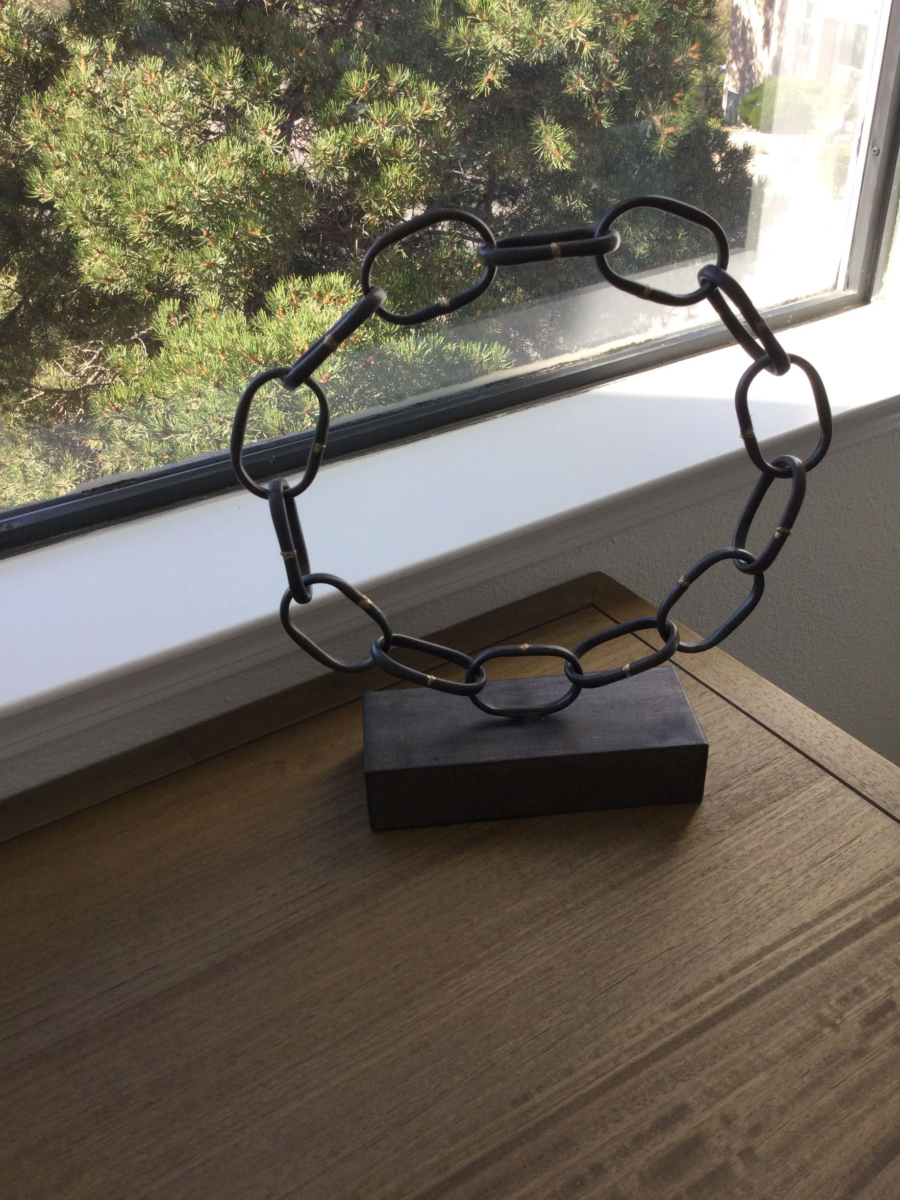 A metal sculpture is sitting on a wooden table in front of a window.