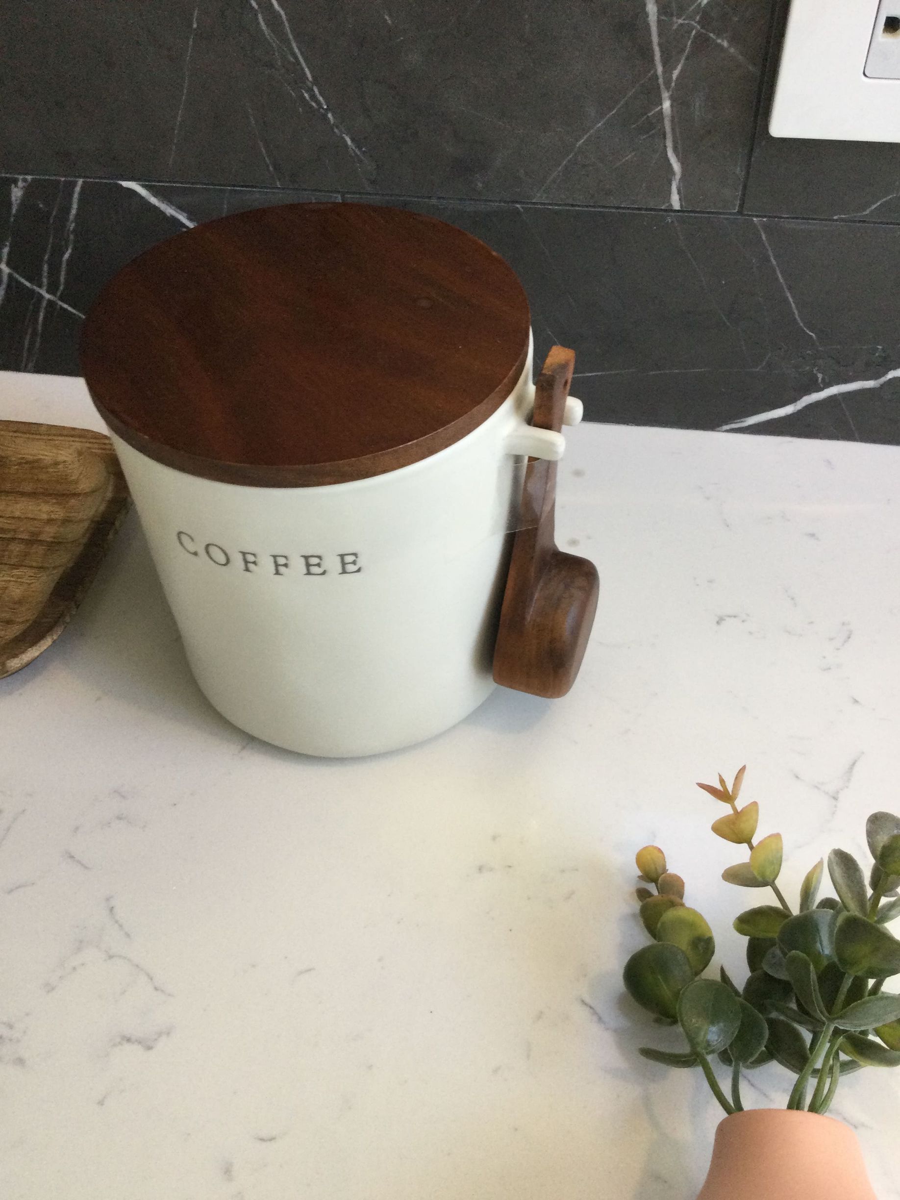 A white coffee container with a wooden lid is on a counter.