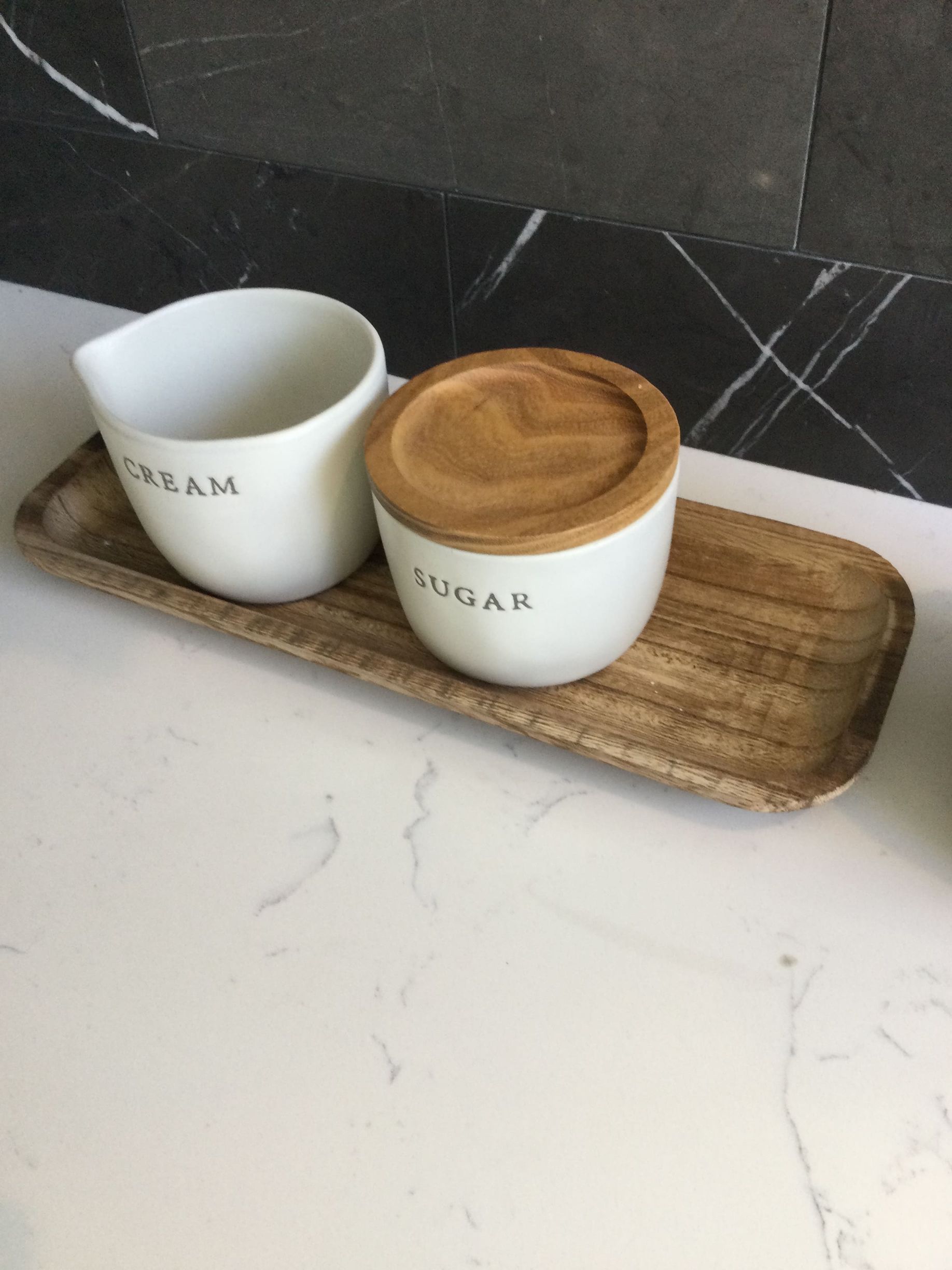 A wooden tray with a sugar bowl and a creamer on it