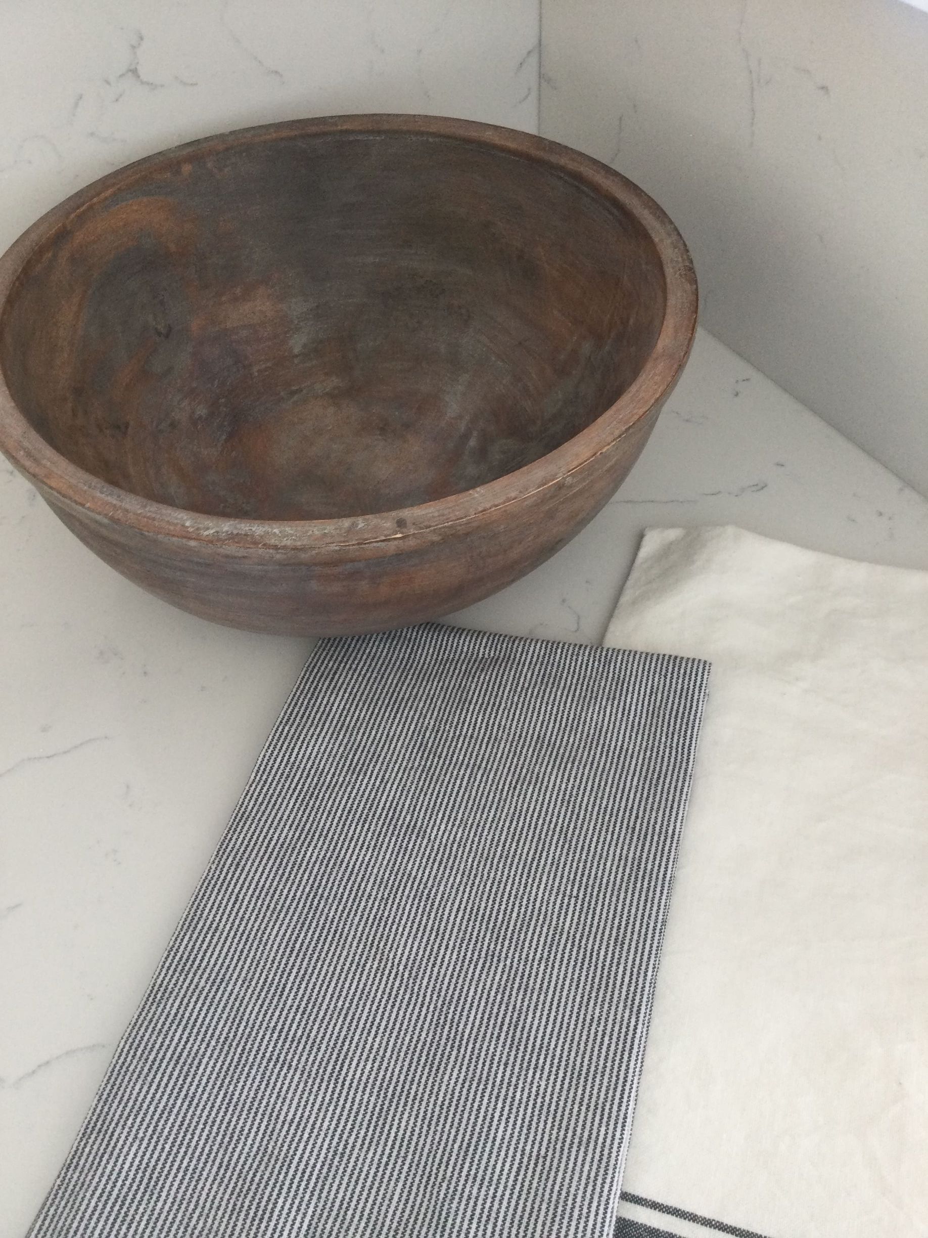 A wooden bowl sits on a counter next to a napkin