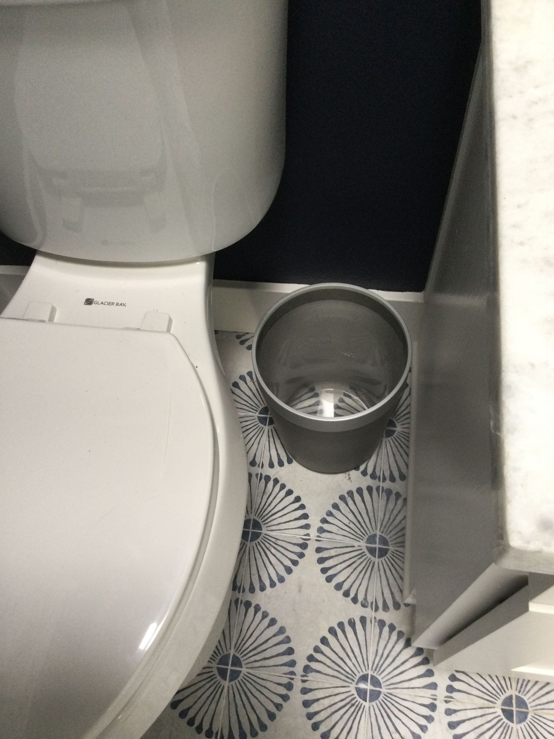 A toilet with a trash can next to it in a bathroom.