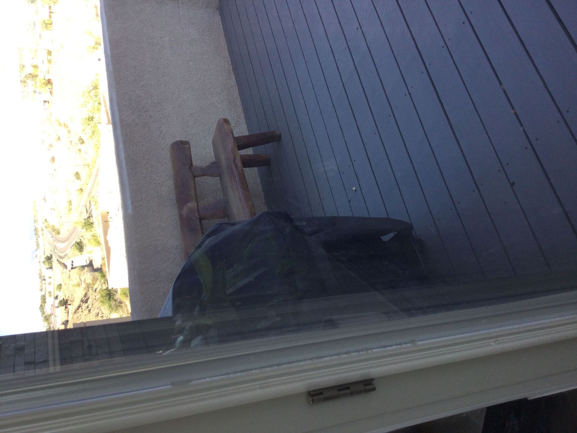 A view of a deck from a window with a chair and a bag on it.
