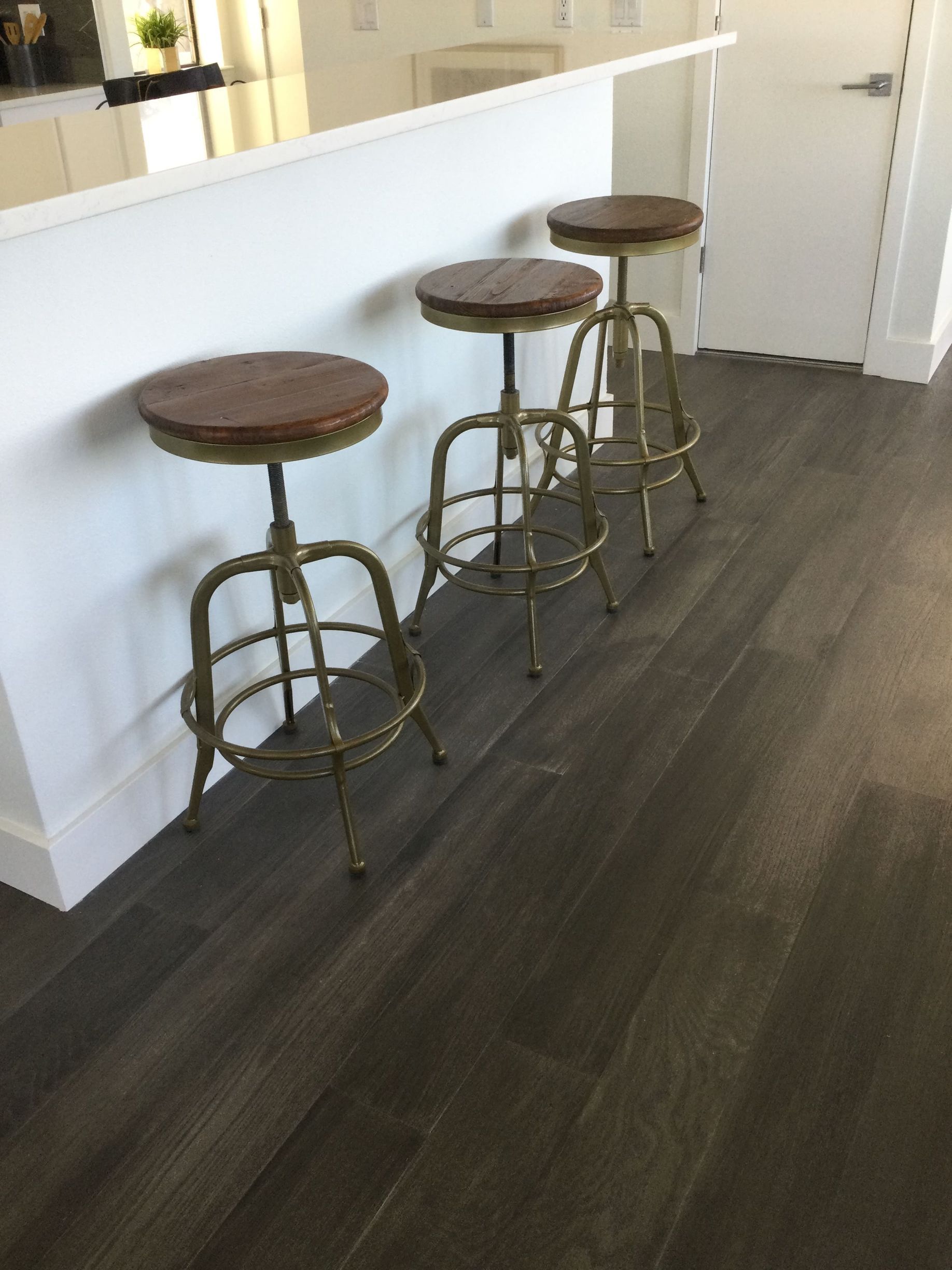 Three bar stools are sitting on a wooden floor in a kitchen.
