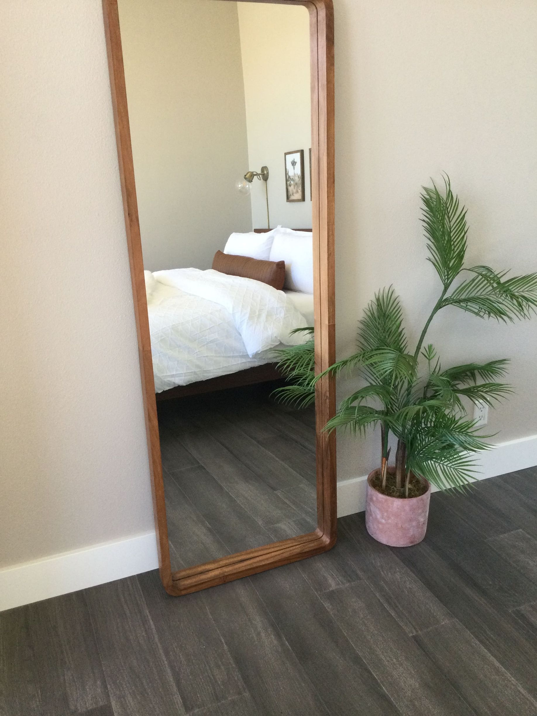 A full length mirror is in a bedroom next to a plant.