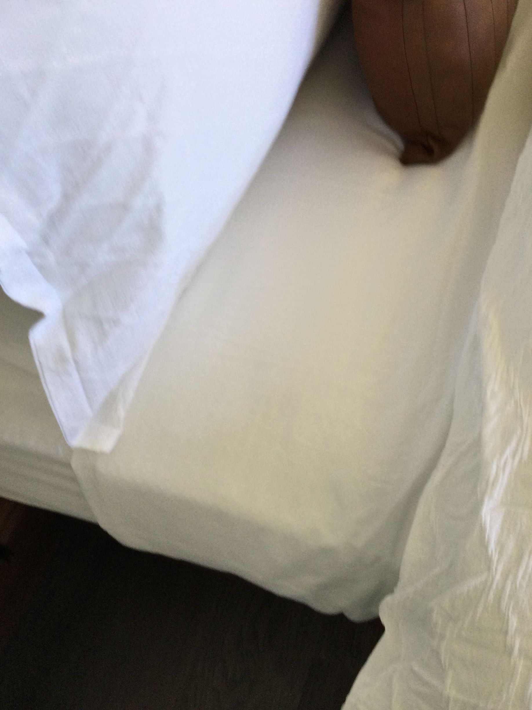 A bed with white sheets and a brown pillow on it.