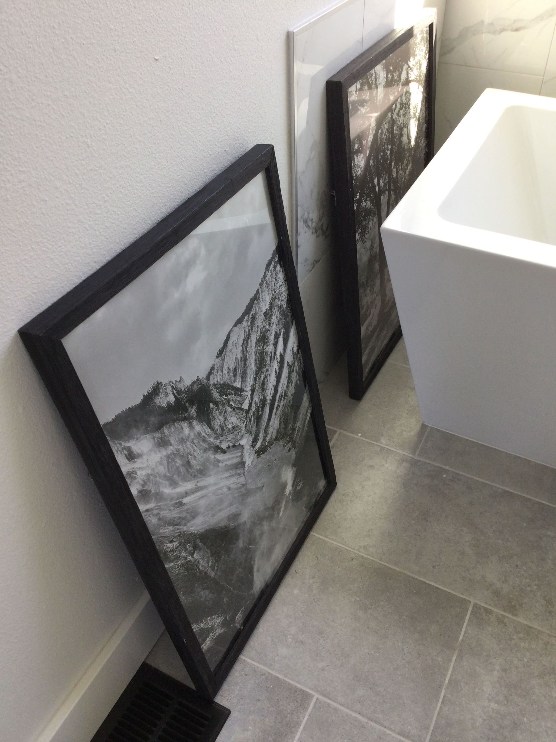 Two framed pictures are on the floor next to a bathtub