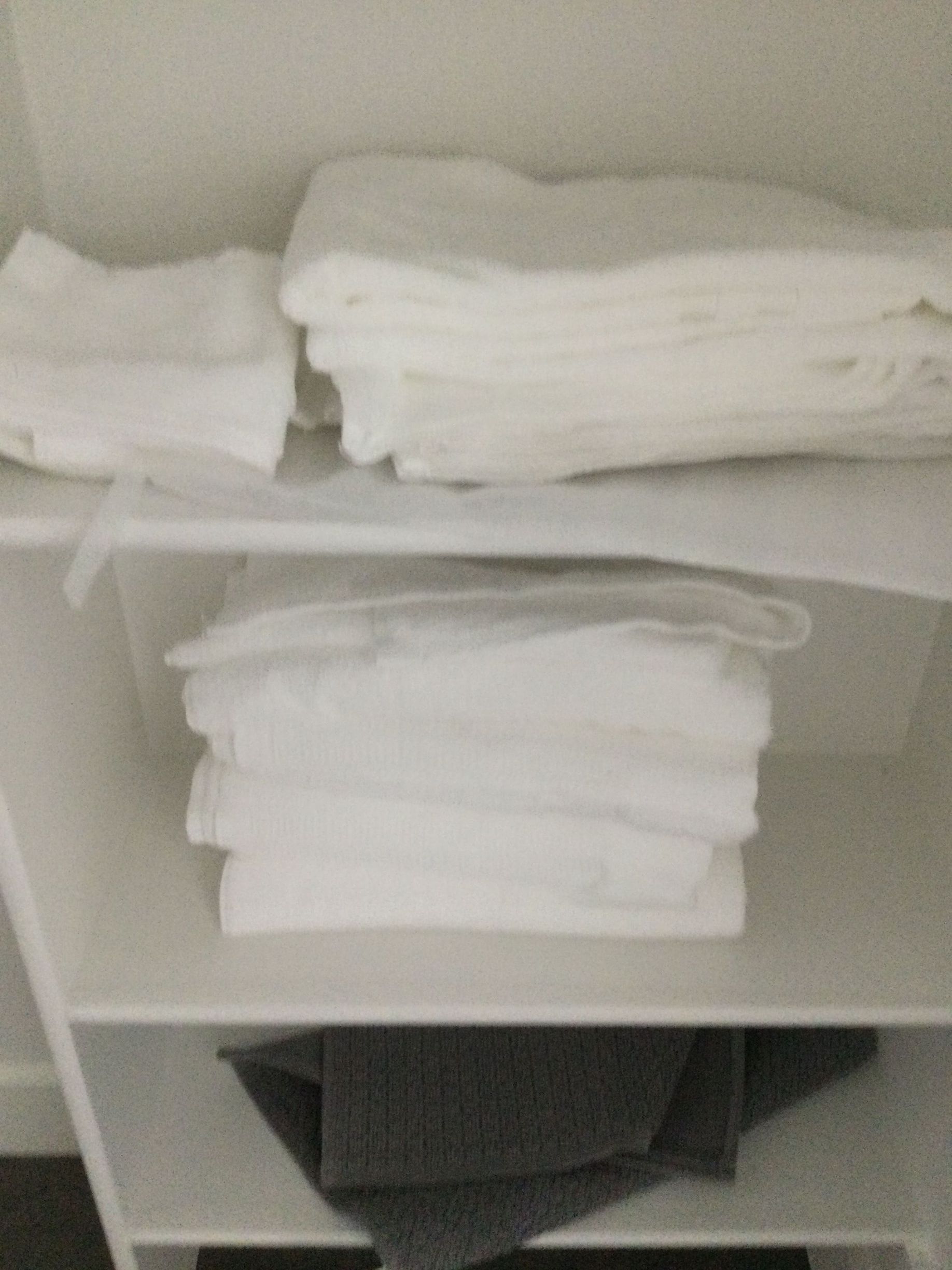 A stack of white towels is sitting on top of a white shelf.
