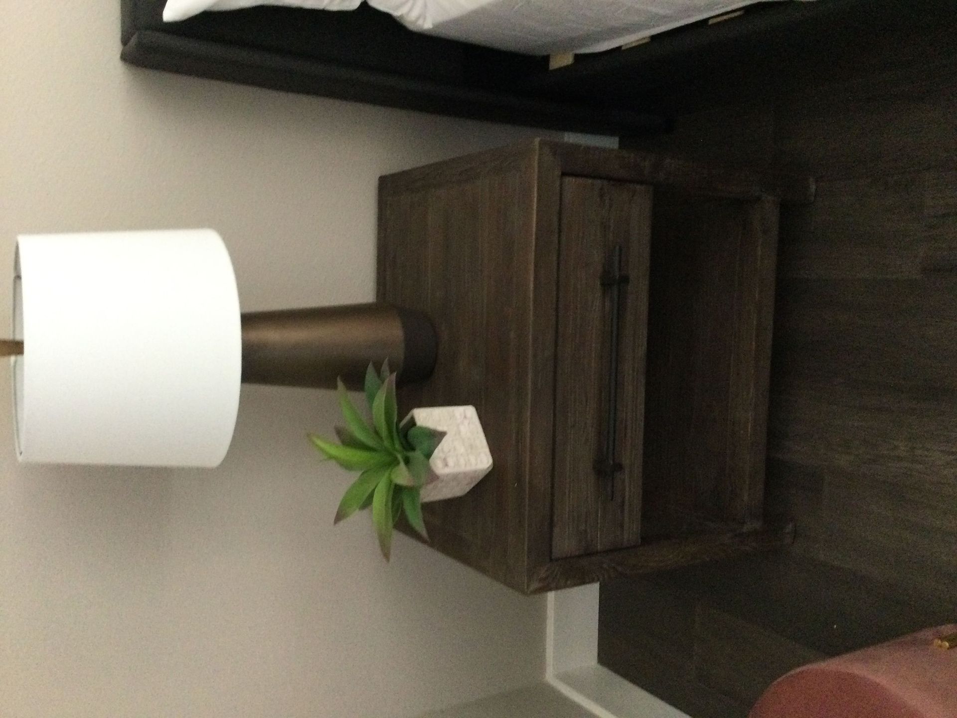 A lamp is sitting on top of a wooden nightstand next to a bed.