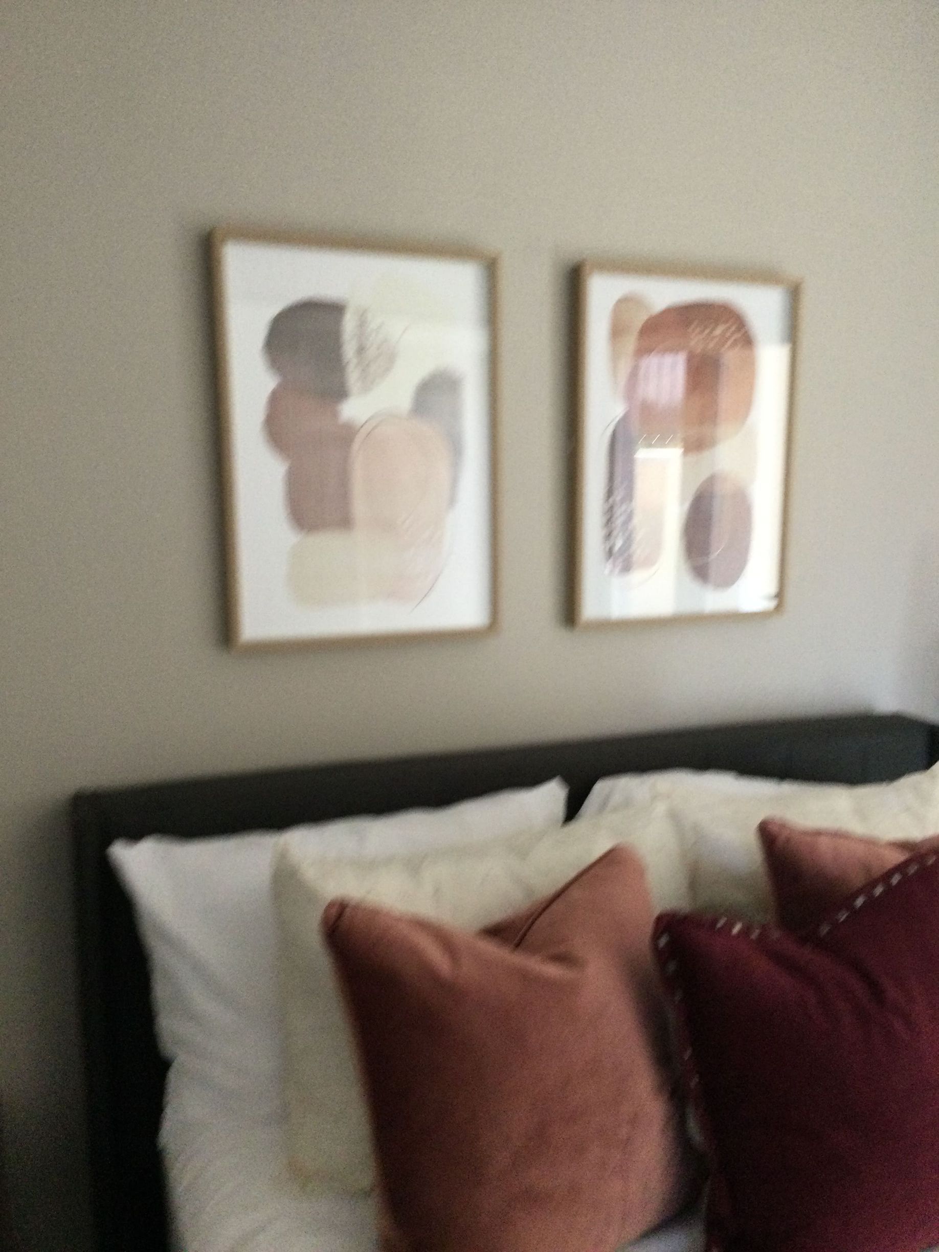 A bed with pillows and two paintings on the wall above it
