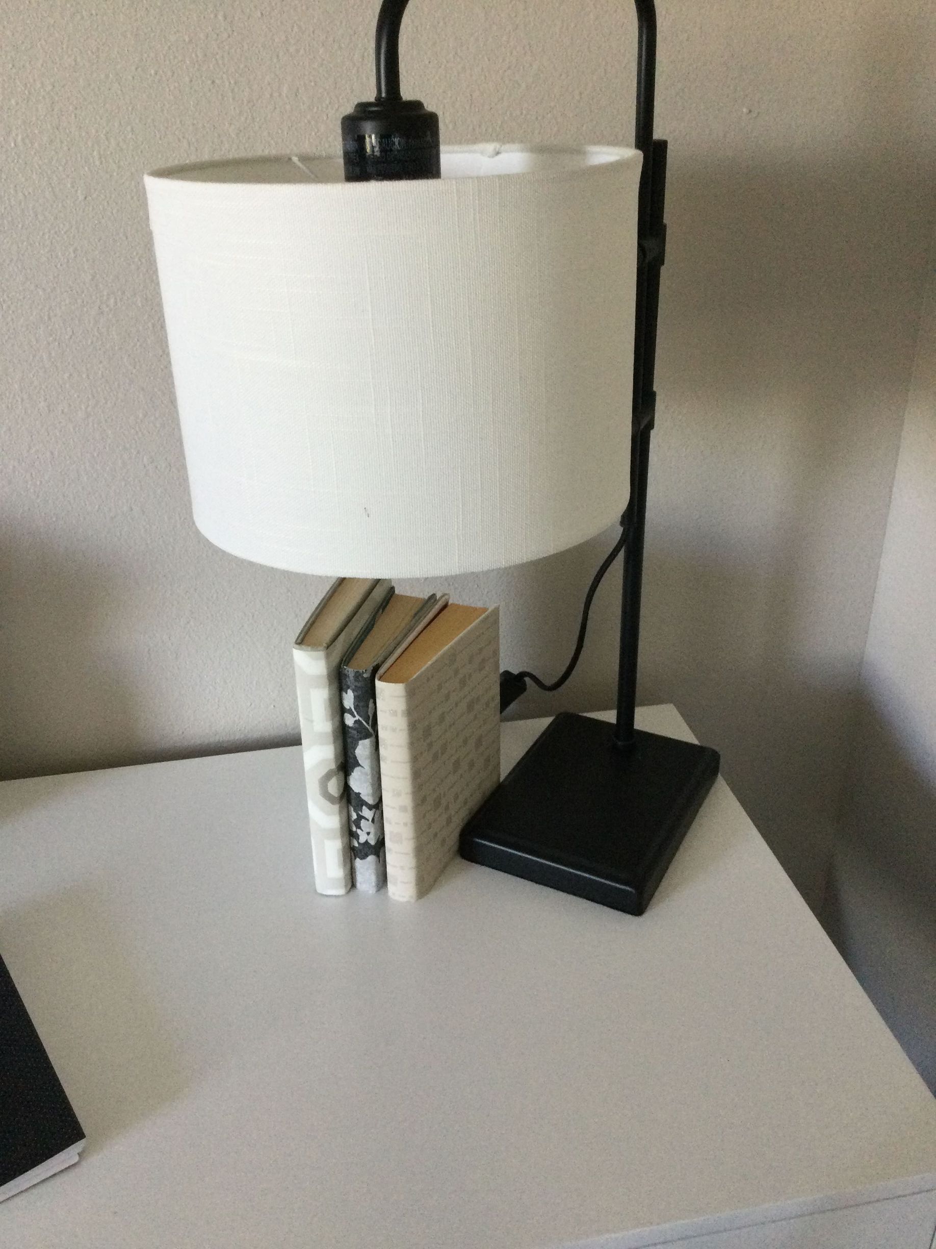 A lamp with a white shade sits on a table next to two books