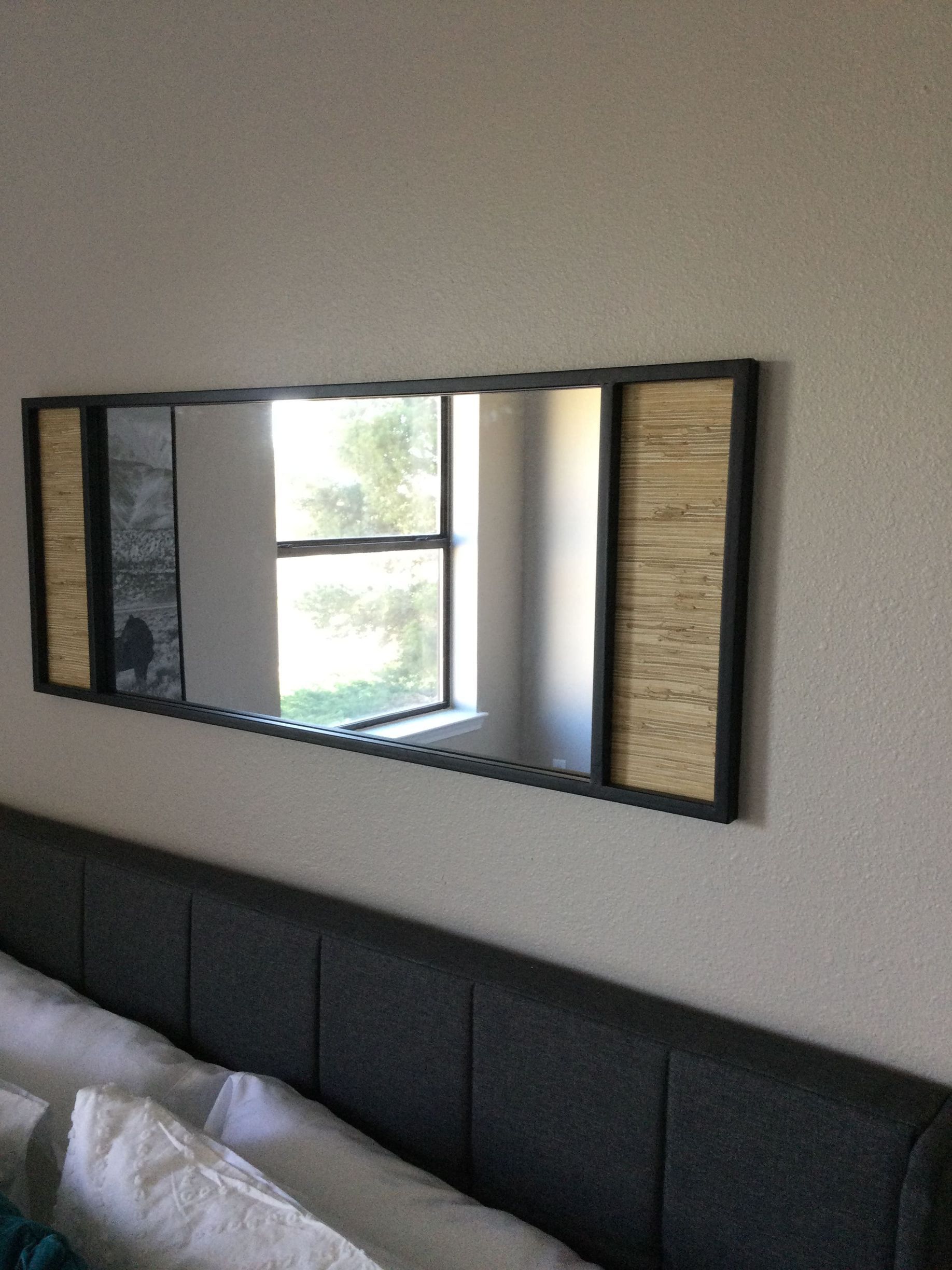 A large mirror is hanging on a wall above a bed.