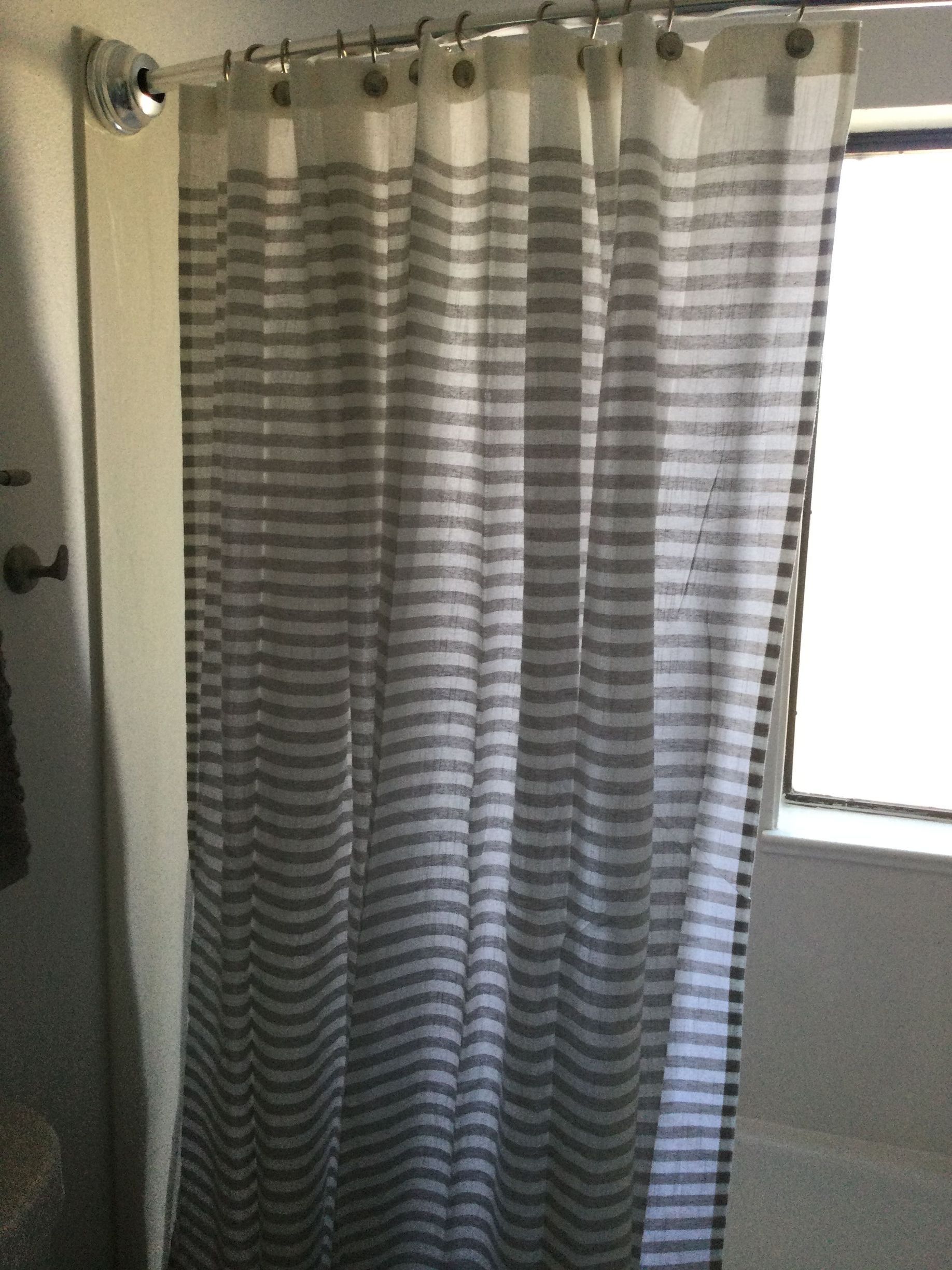 A striped shower curtain hangs in a bathroom next to a window