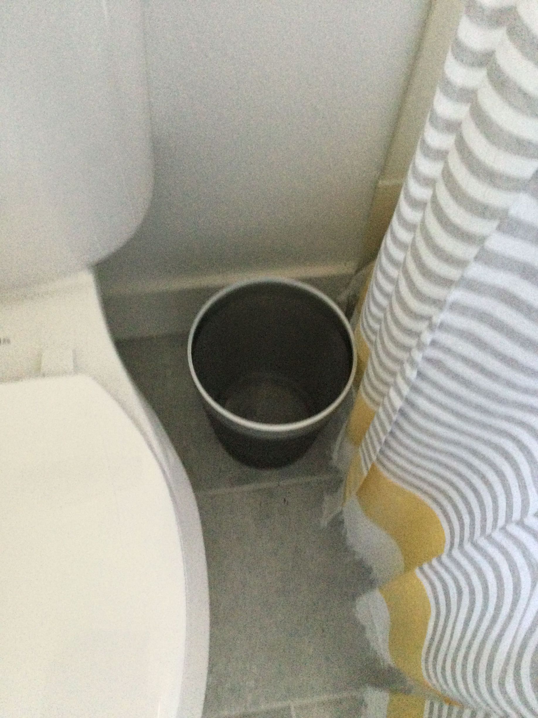 A toilet and a trash can in a bathroom next to a shower curtain.