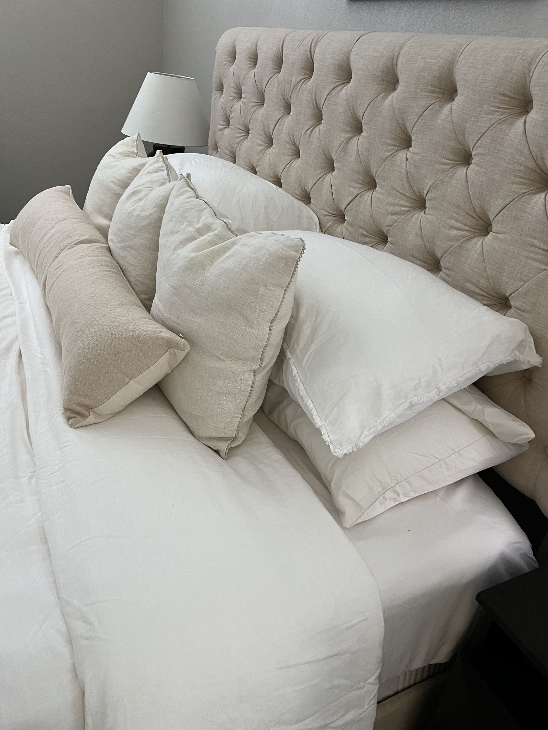 A bed with white sheets and pillows and a tufted headboard.