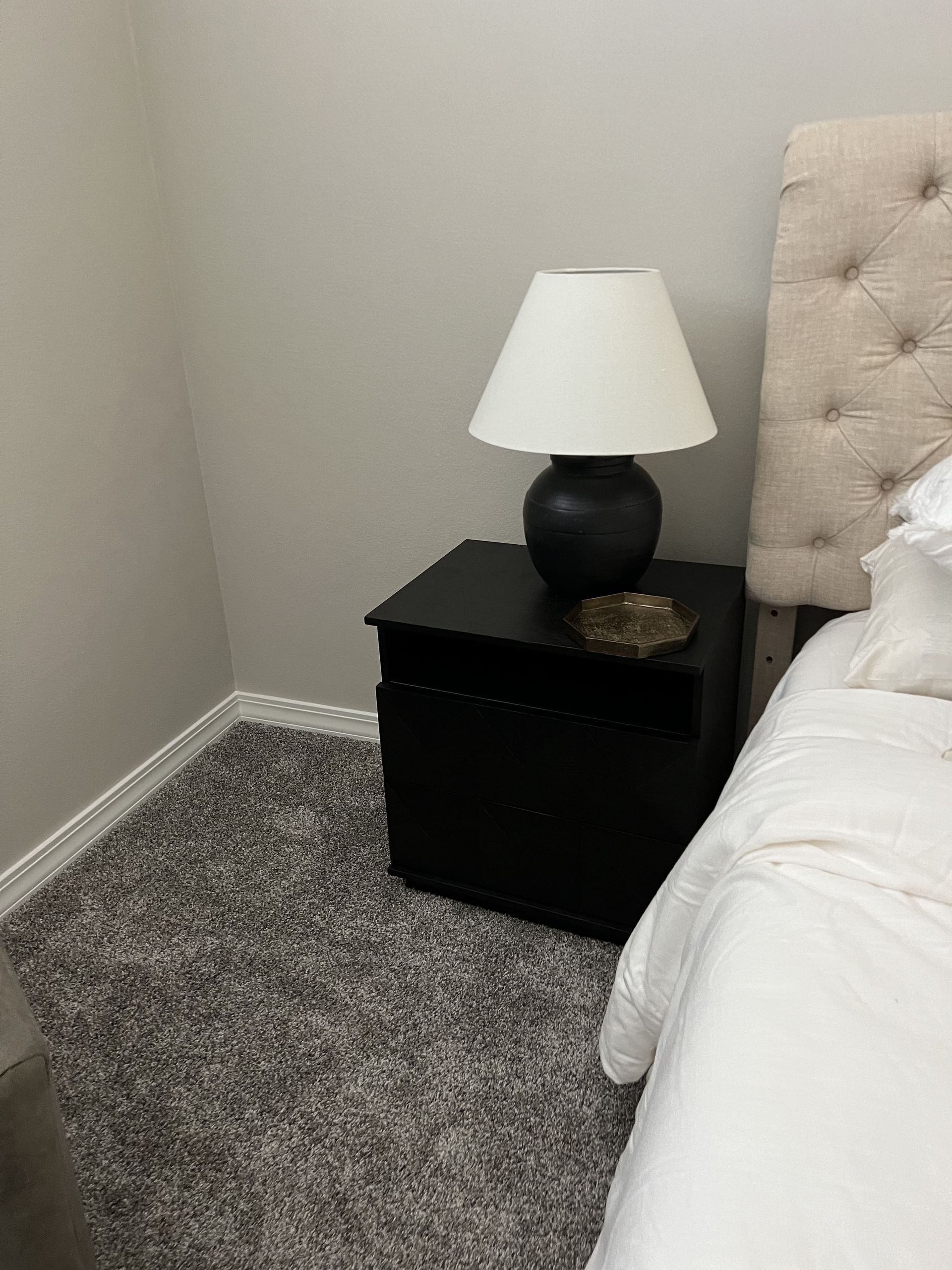 A bedroom with a bed , nightstand , lamp and carpet.
