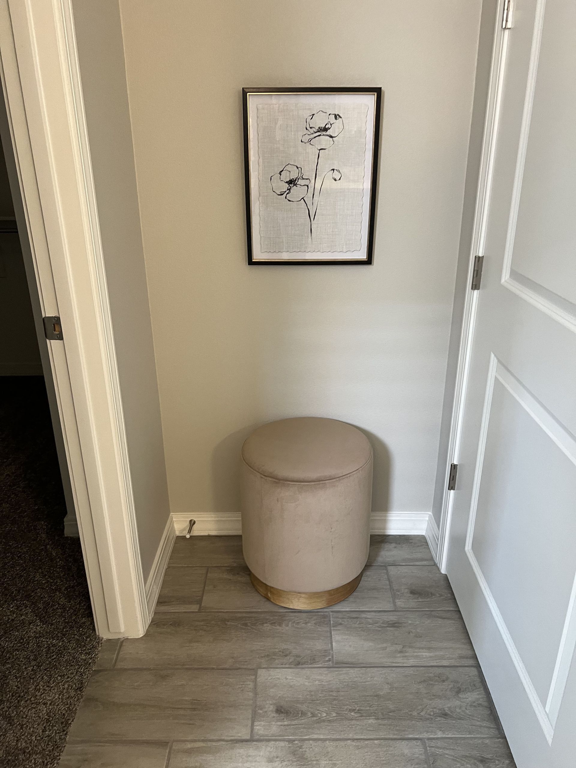 A ottoman is sitting in a corner of a room next to a door.