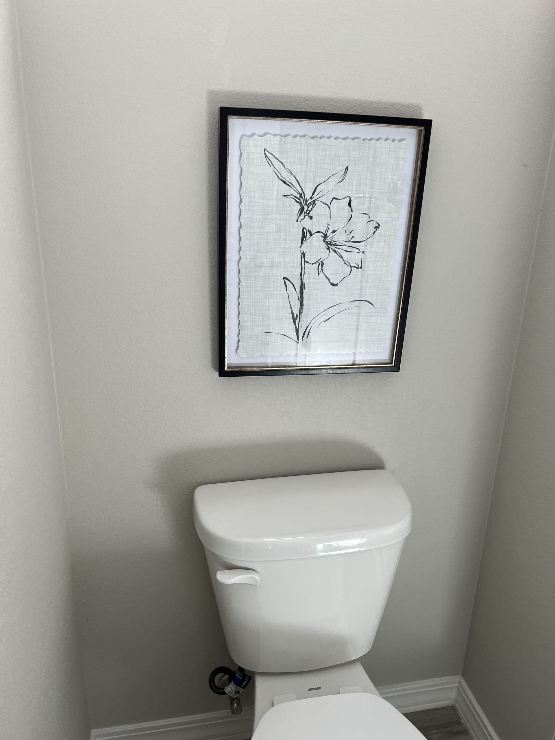 A toilet in a bathroom with a picture on the wall above it.