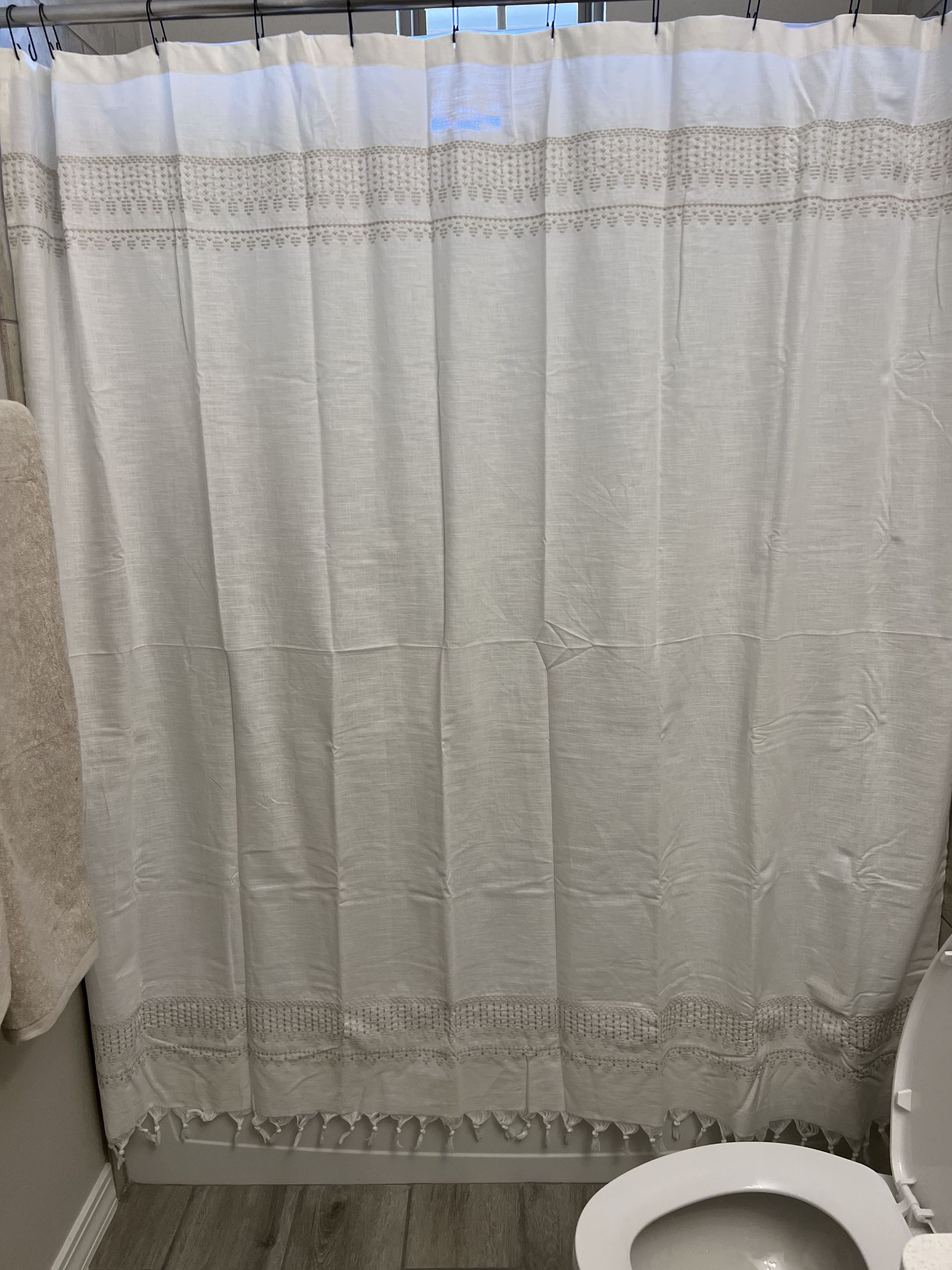 A white shower curtain is hanging in a bathroom next to a toilet.