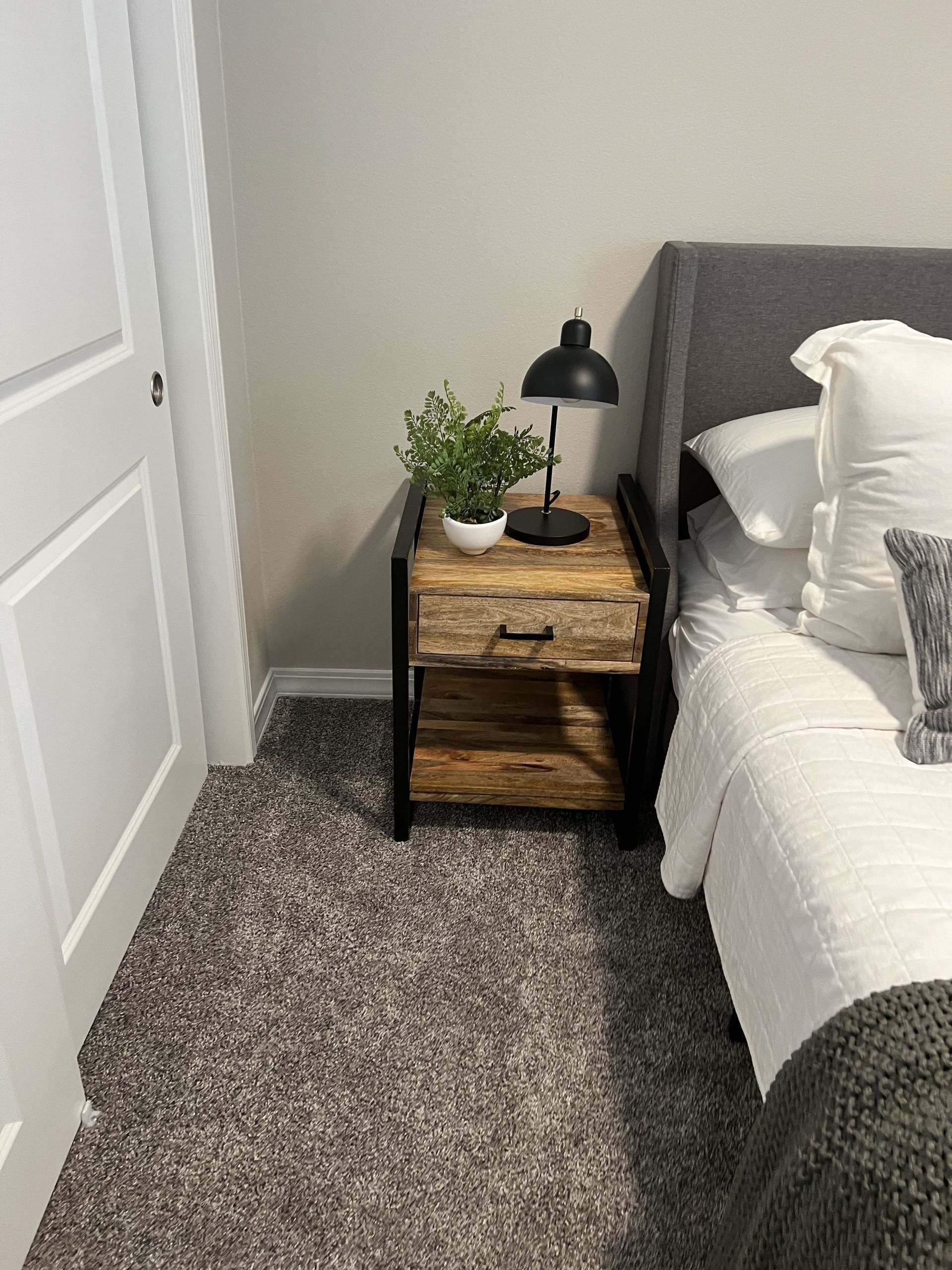 A bedroom with a bed , nightstand , lamp and carpet.
