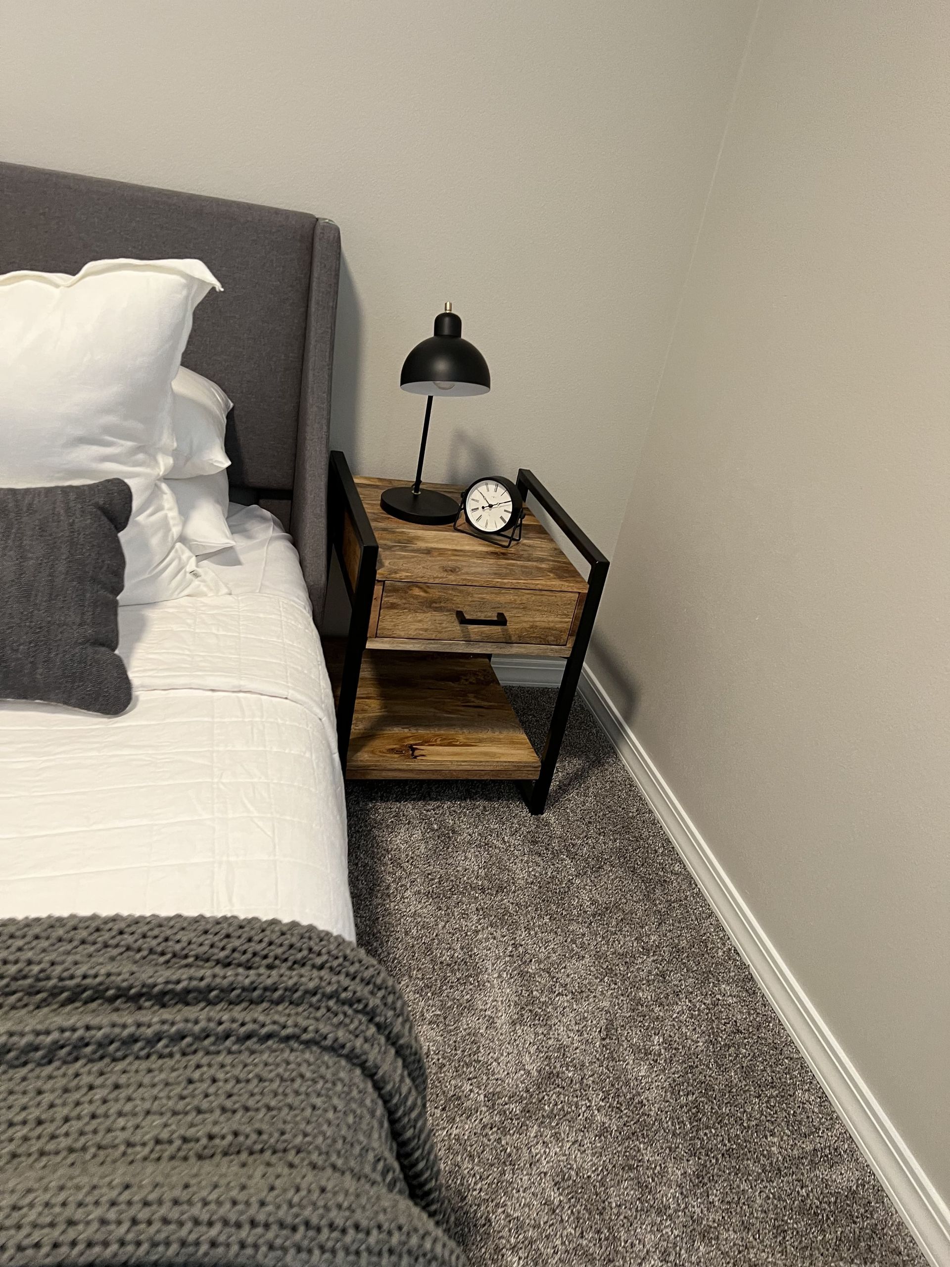 A bedroom with a bed , nightstand , lamp and carpet.