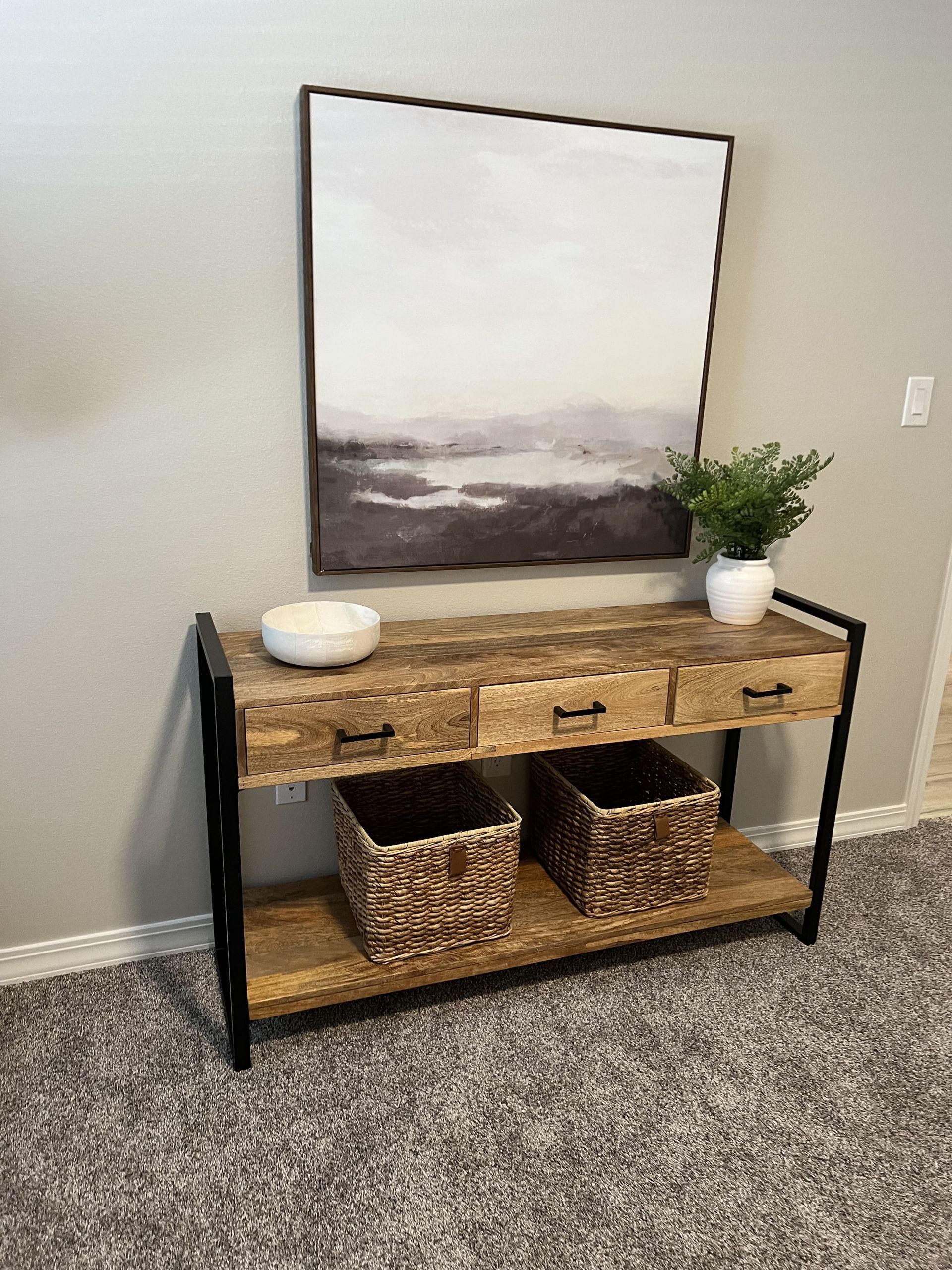 A wooden console table with baskets and a painting on the wall.