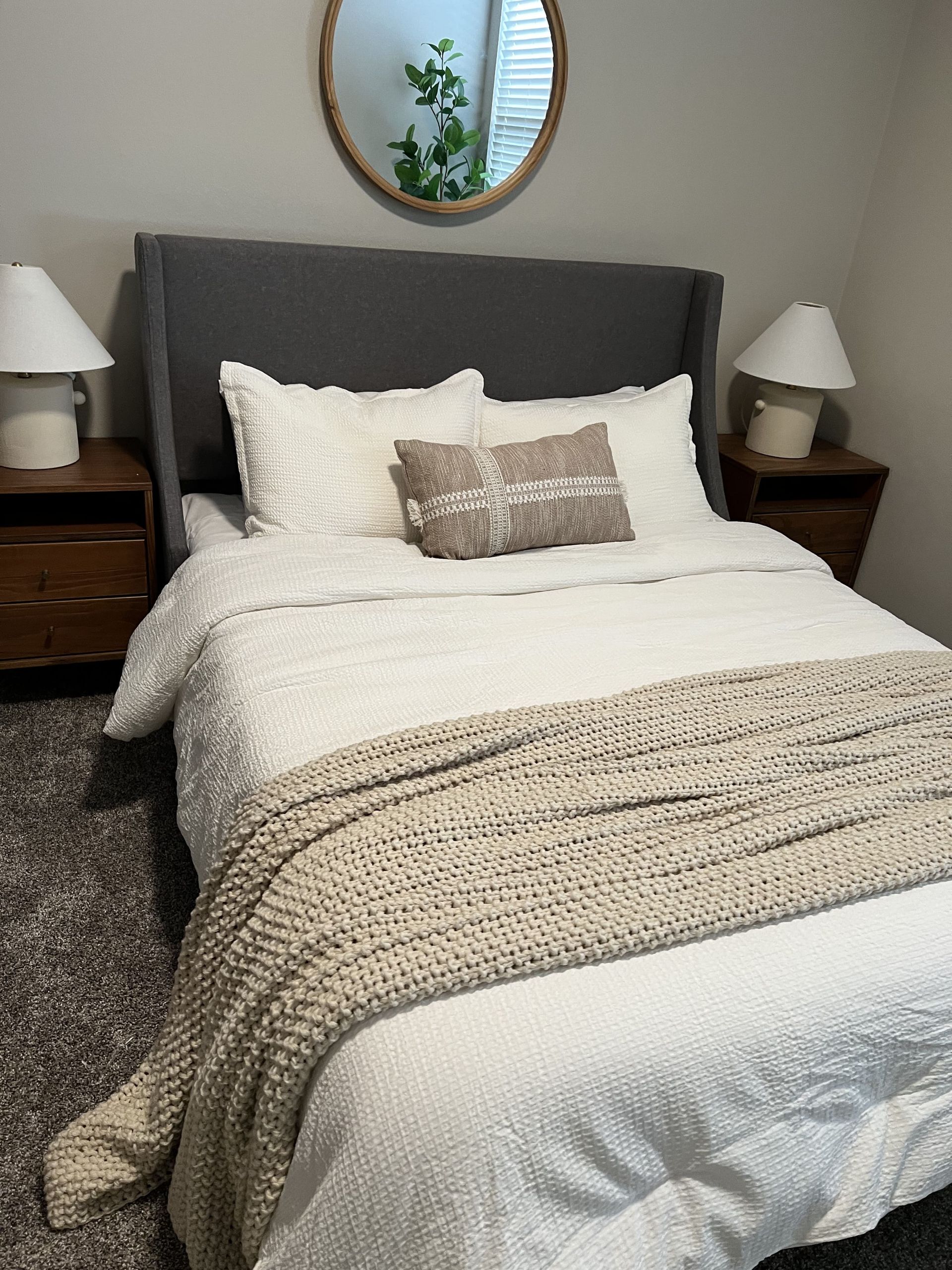 A bedroom with a bed , nightstands , lamps and a mirror.