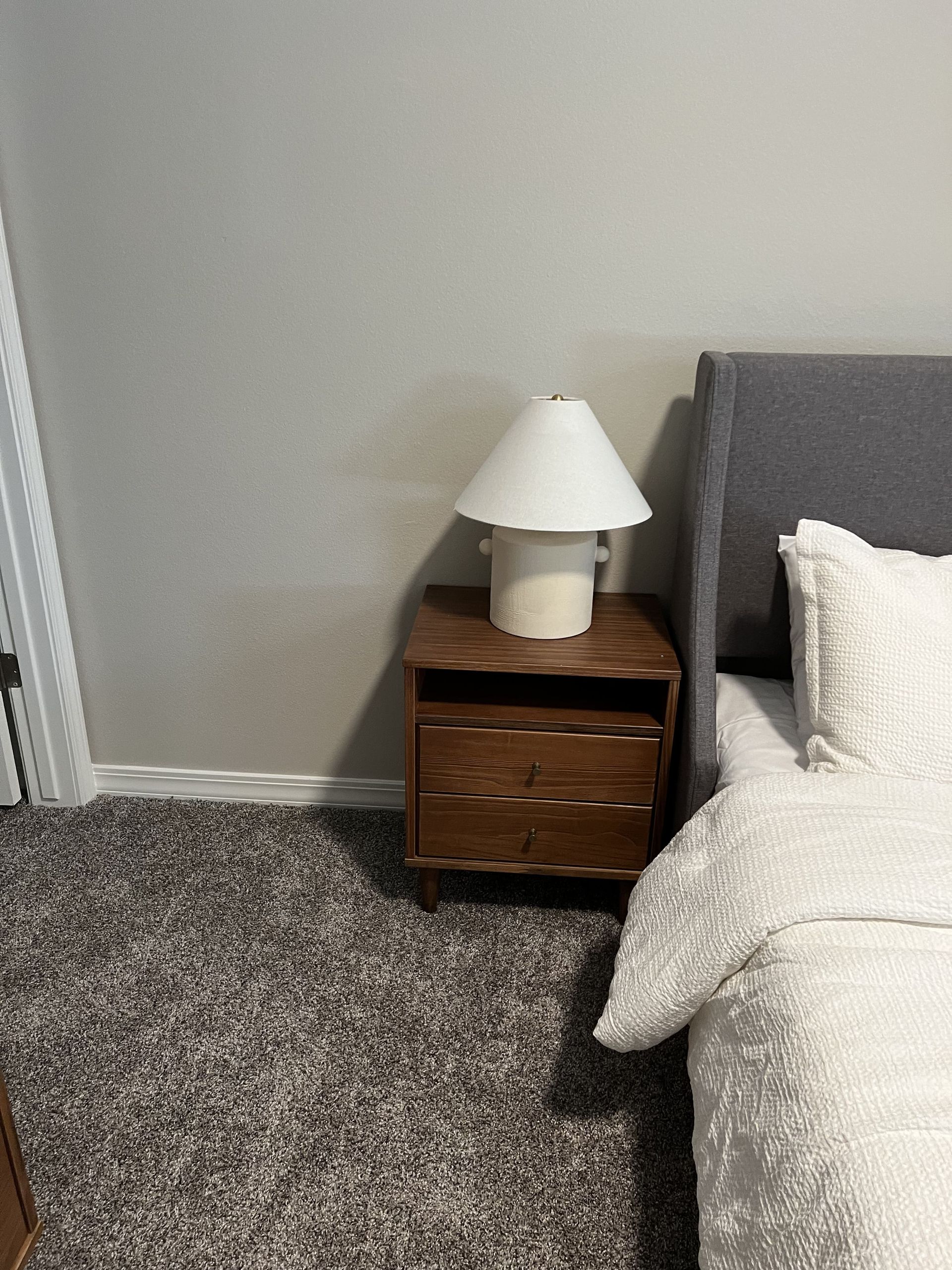A bedroom with a bed , nightstand , lamp and carpet.