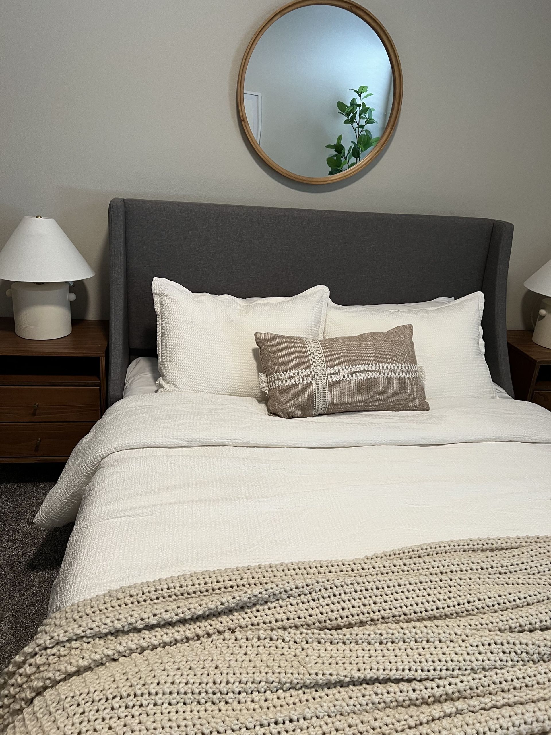 A bed with white sheets and pillows in a bedroom with a round mirror on the wall.
