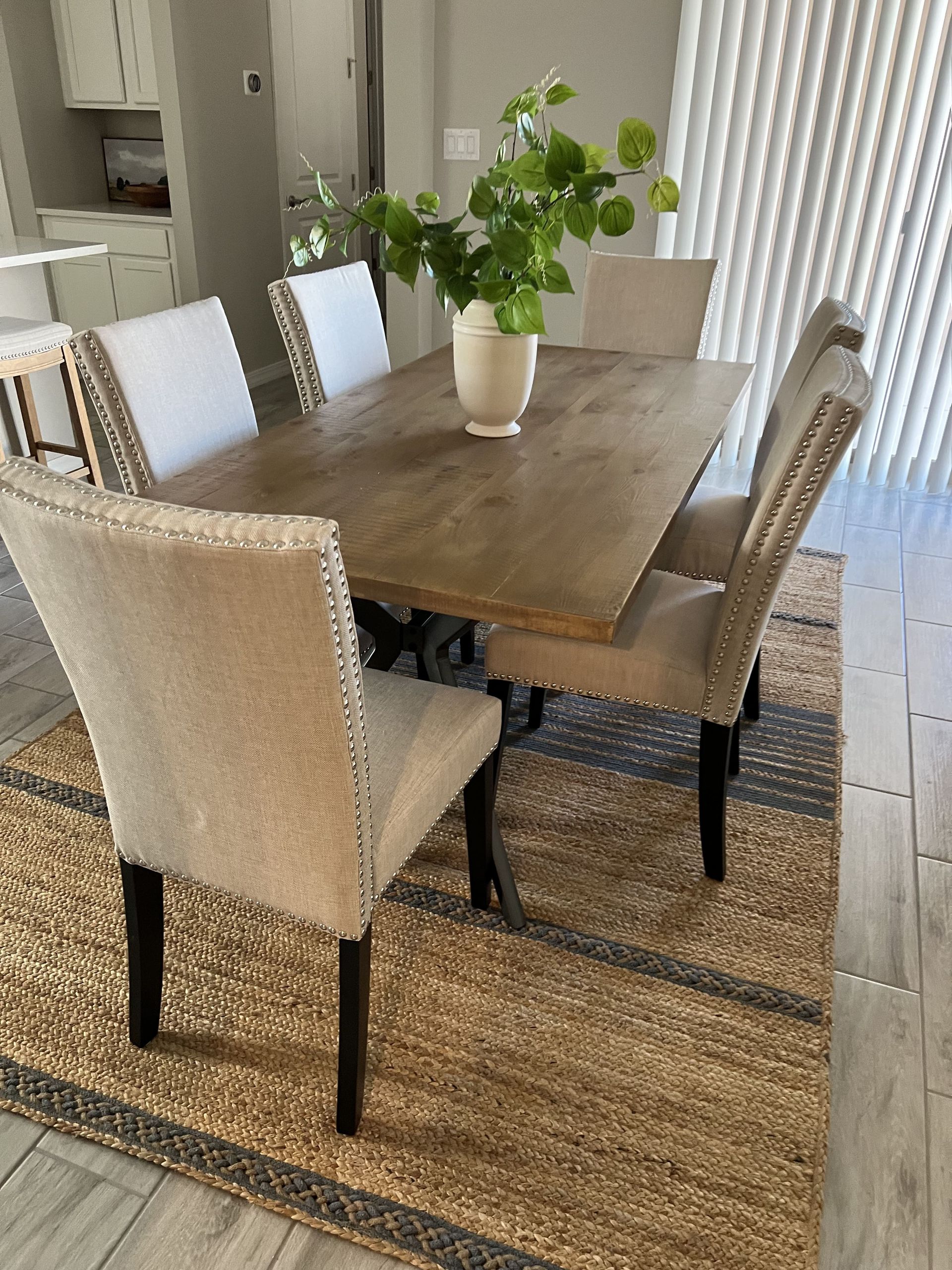 A dining room table with chairs and a rug on the floor.